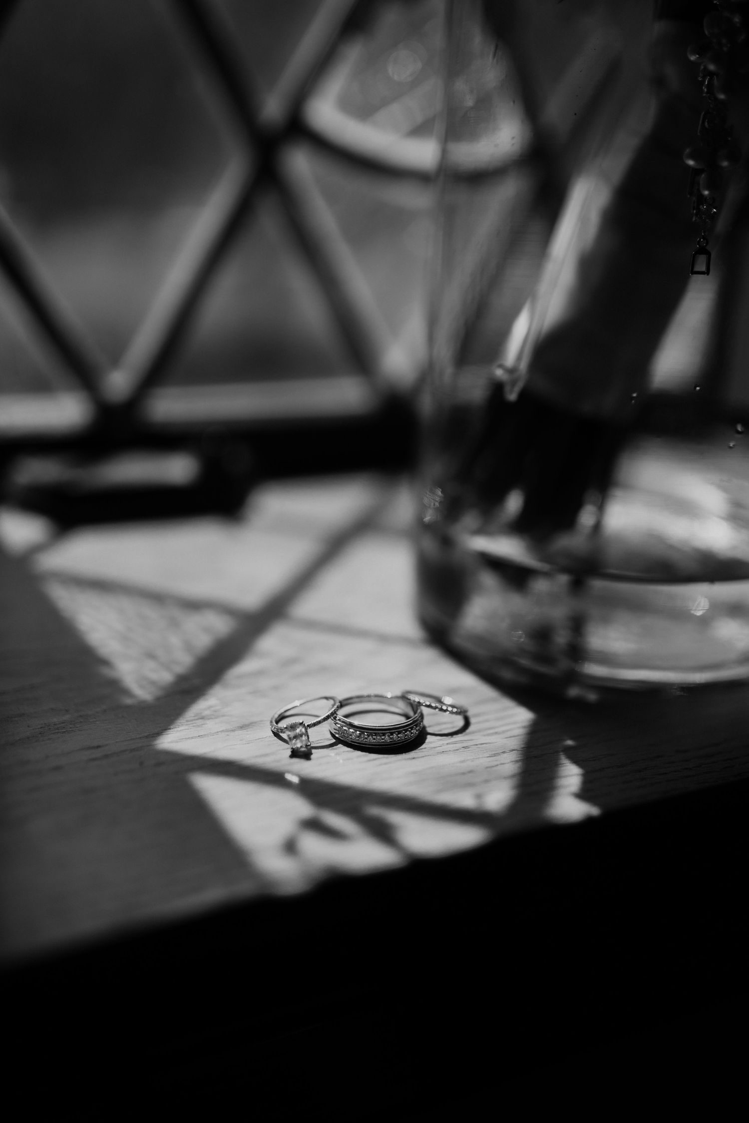 Wedding rings and shadows cast dramatic lighting on a wooden surface in black and white.