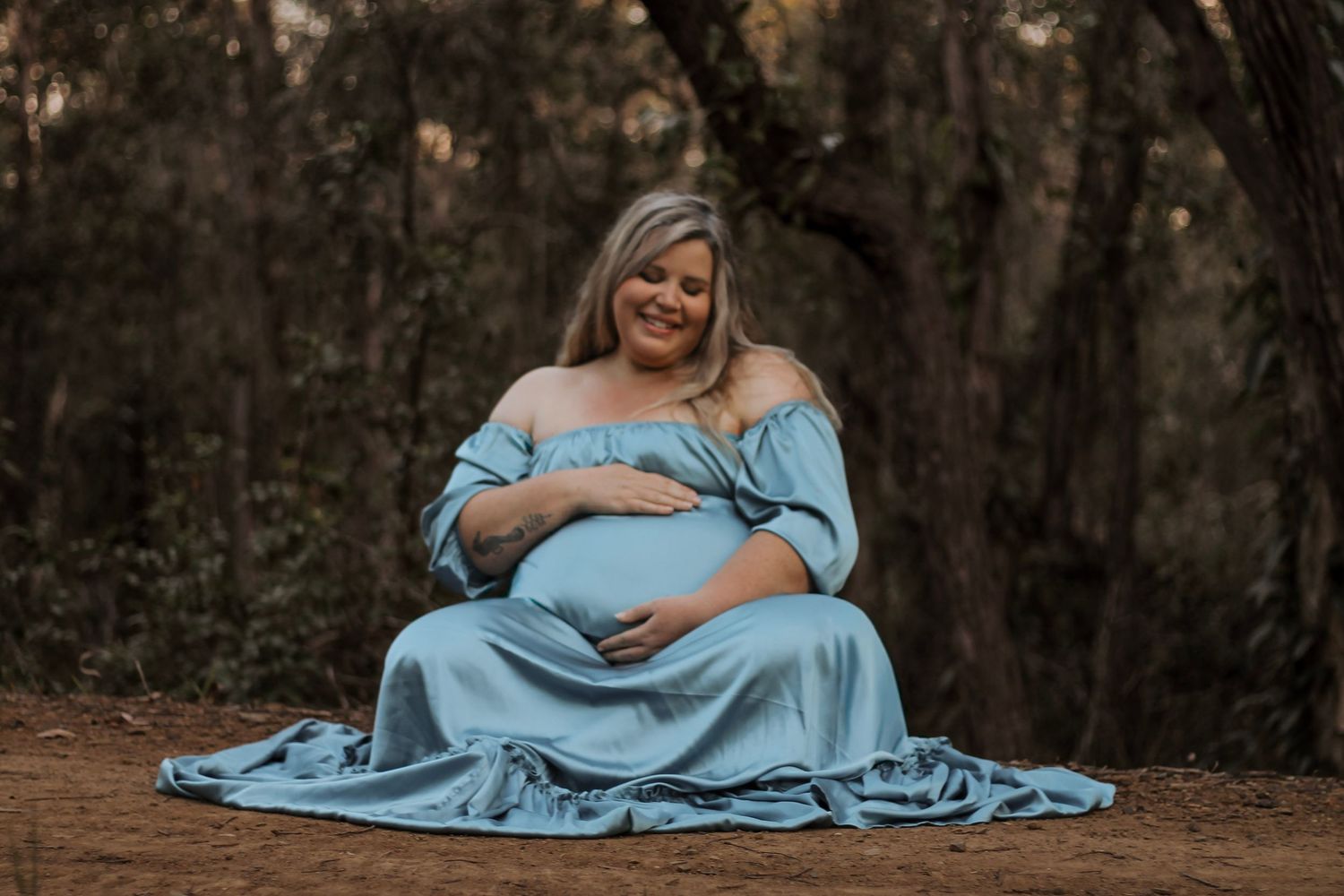 Pregnant mother Sitting in beautiful bushland during sunset maternity photography session in Hervey Bay.
