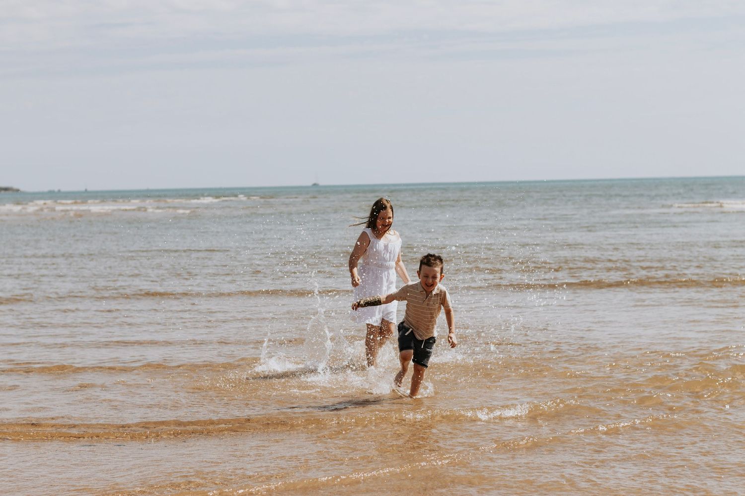 Two siblings chasing each other along the beach during a morning family photography session in Hervey Bay.