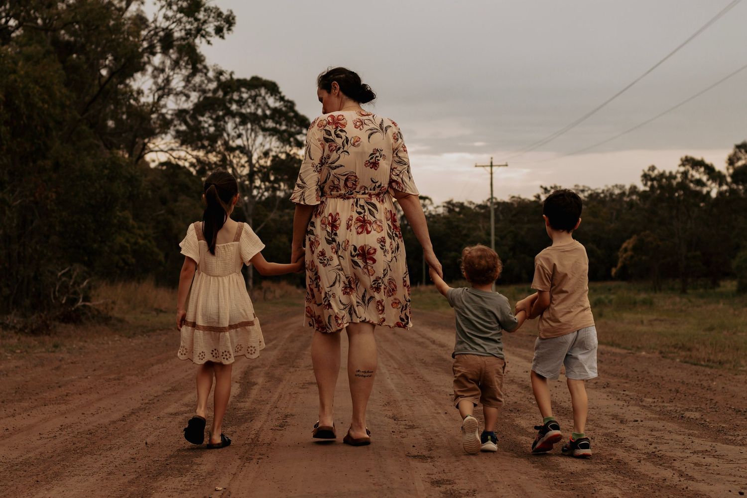 Mother with her 3 young children walking hand in hand along the bushland during a sunset family photography session in Hervey Bay.