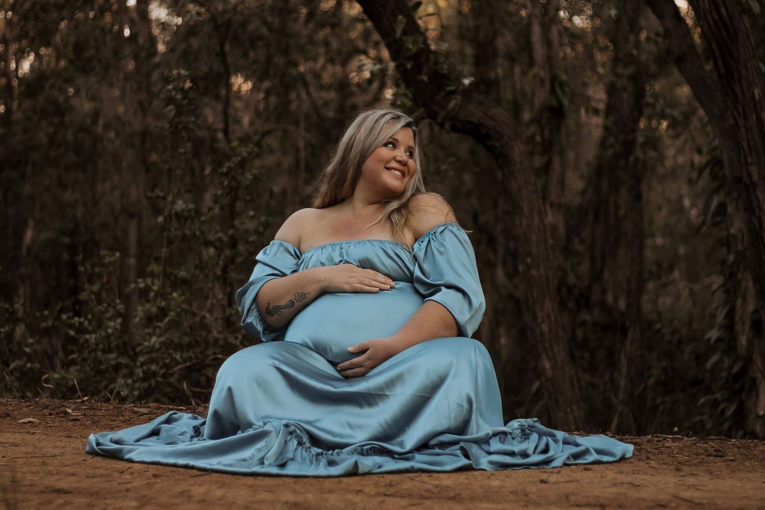 Pregnant mother Sitting in beautiful bushland during sunset maternity photography session in Hervey Bay.