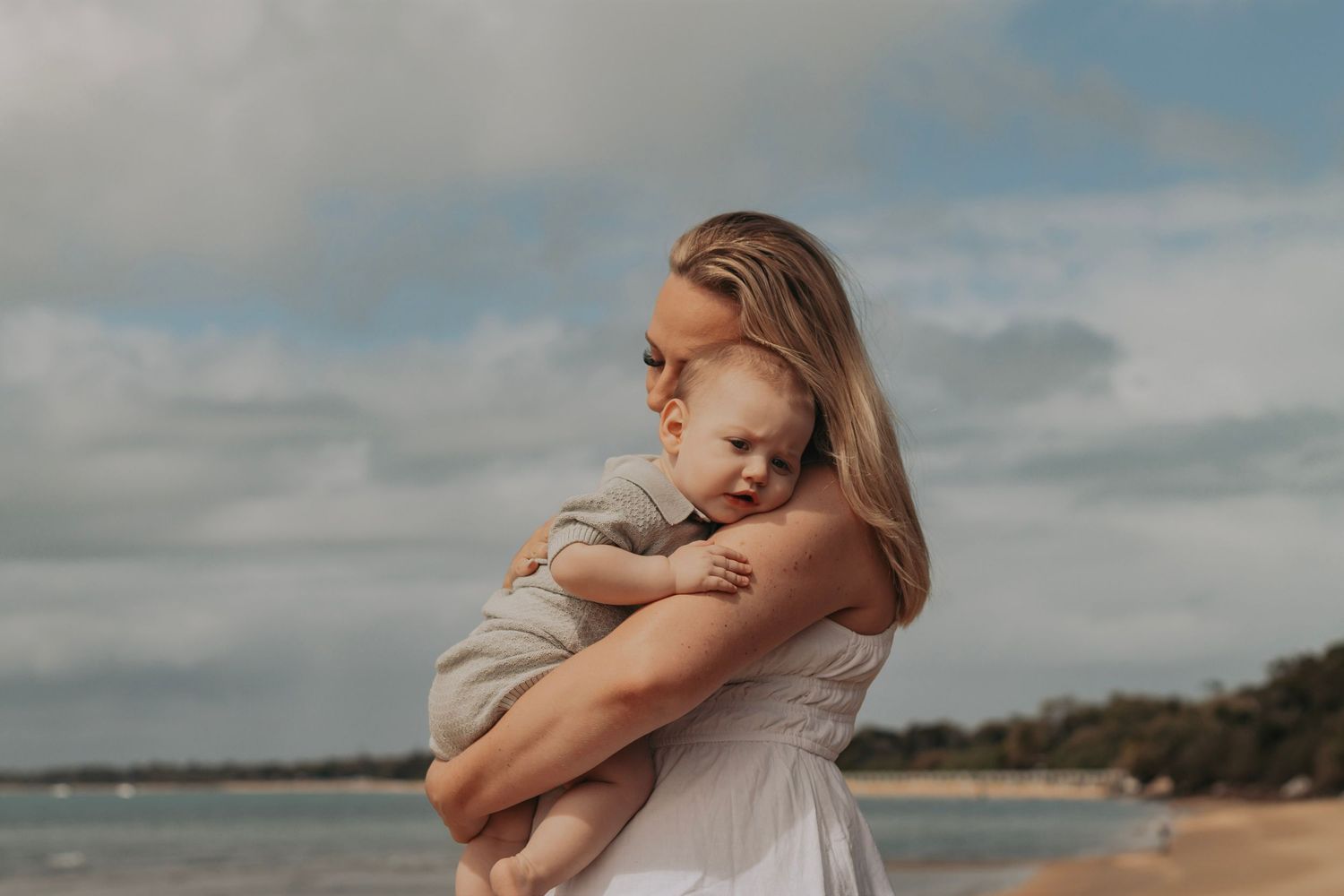 Little boy getting Mum cuddles at his first time at the beach in the morning. Motherhood Photographer