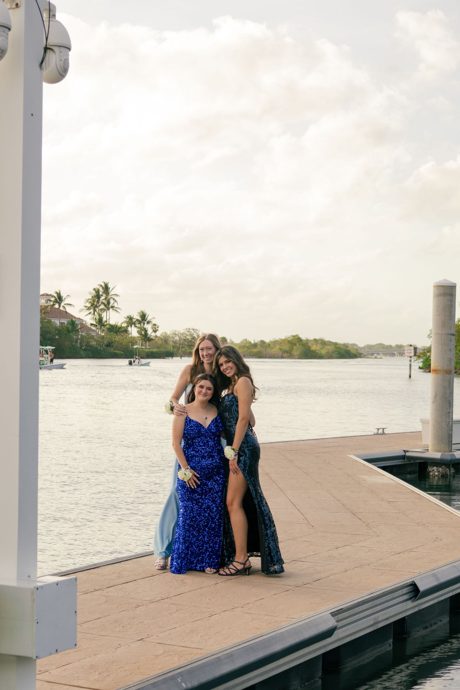 Three young women in blue sequin prom dresses posing on a dock by the water.