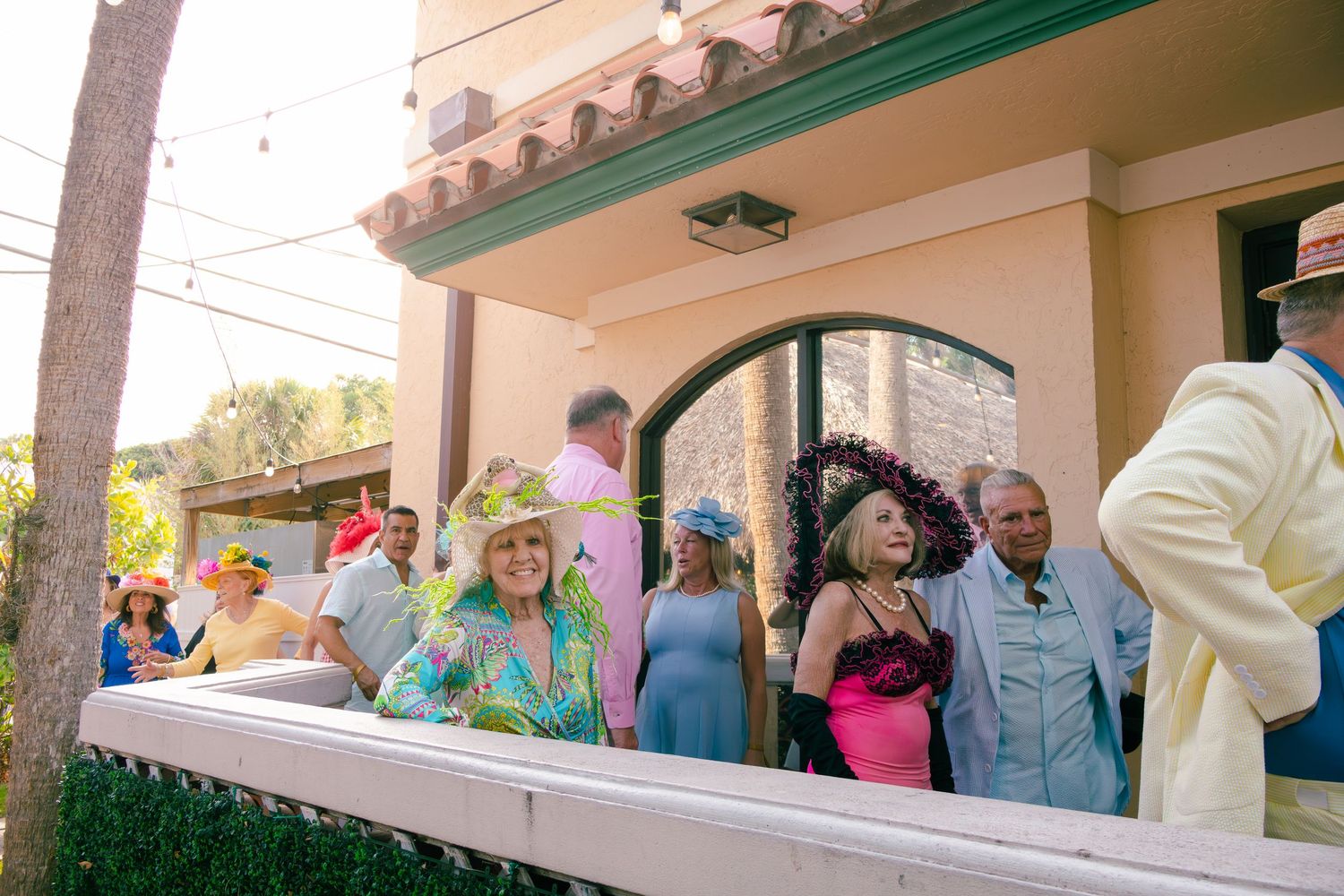 Guests in elaborate colorful Kentucky Derby hats gathered at a festive outdoor party.