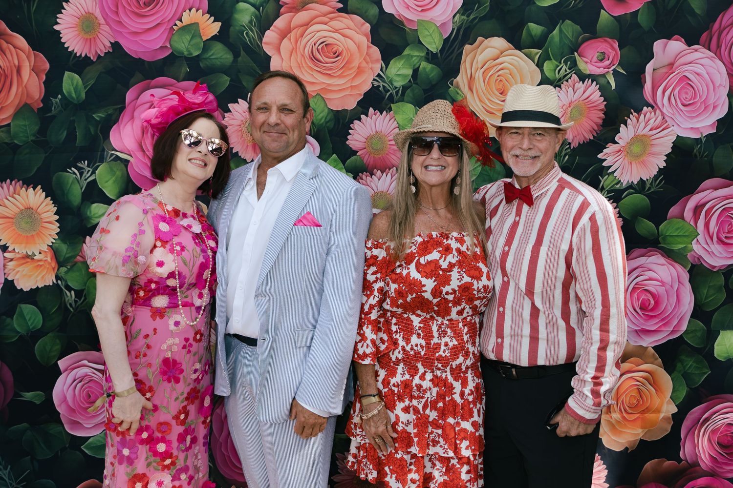 Four elegantly dressed guests posing together in front of a vibrant floral backdrop at a Derby party.