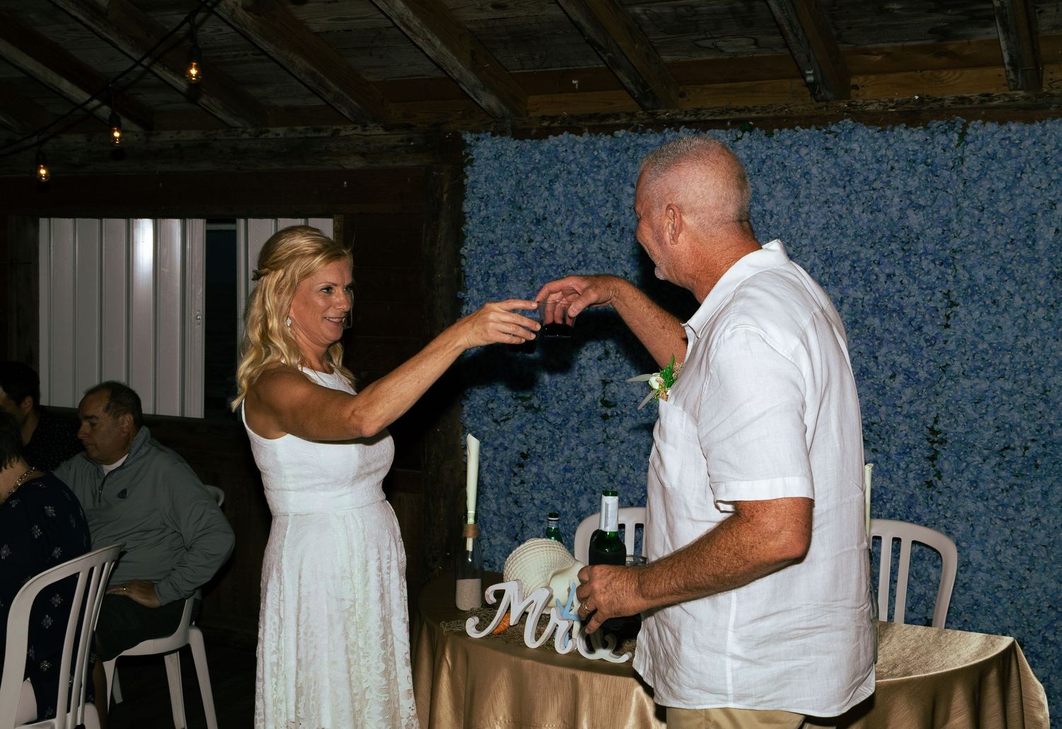 Bride feeding wedding cake to groom at elegant reception table decorated with white flowers.