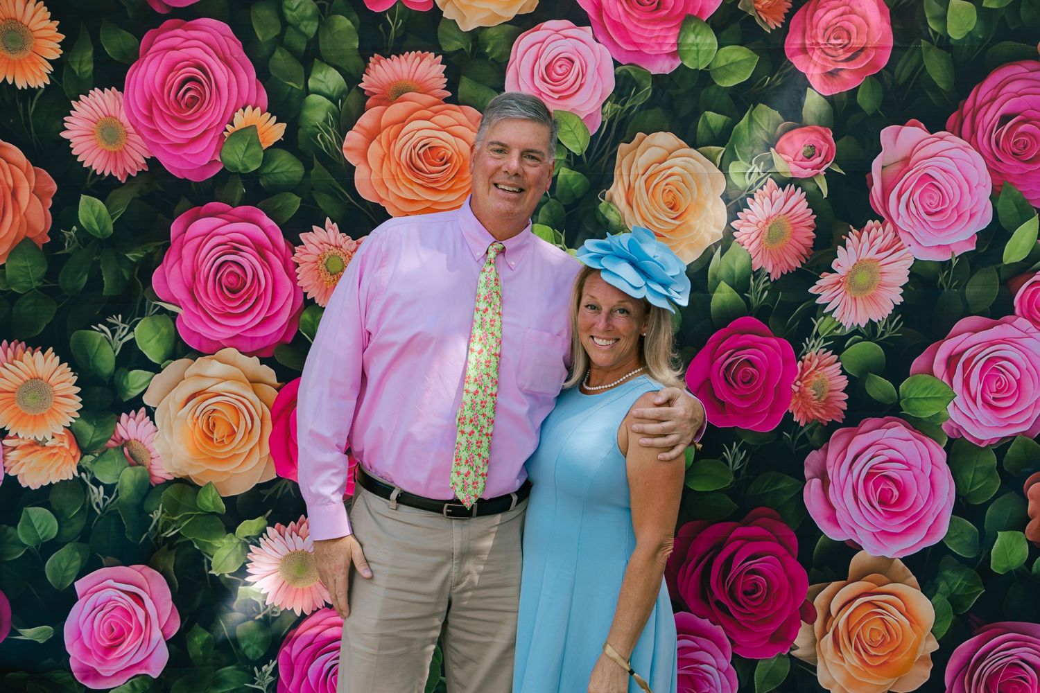 Couple posing in front of a vibrant floral rose backdrop at a Kentucky Derby themed party.