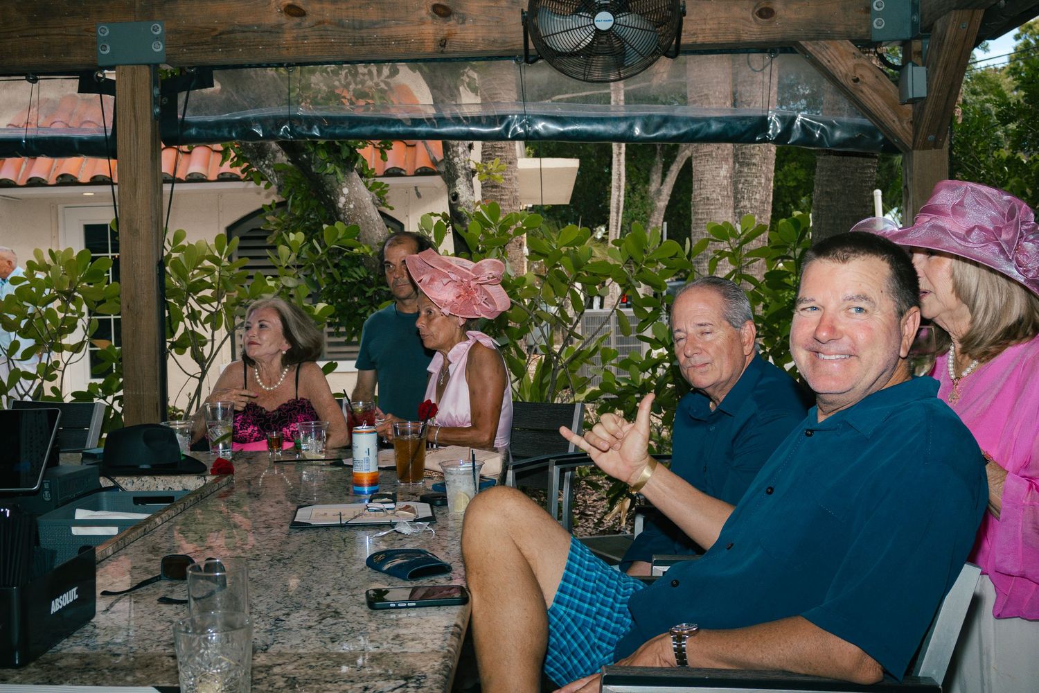 Happy guests in colorful hats laugh and clap at an outdoor covered patio party.