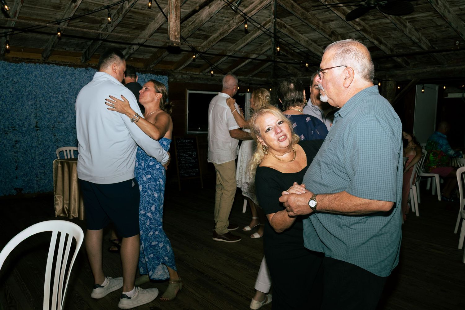 Smiling woman dances with older man at rustic indoor wedding reception.
