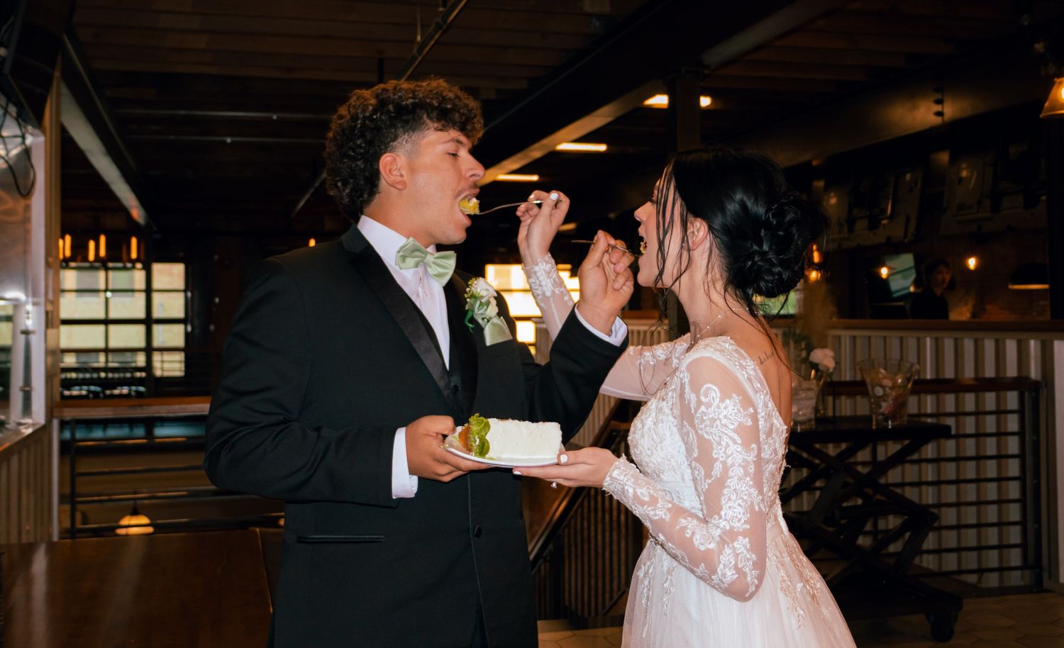 Bride feeds groom wedding cake during fun cake cutting ceremony at reception.