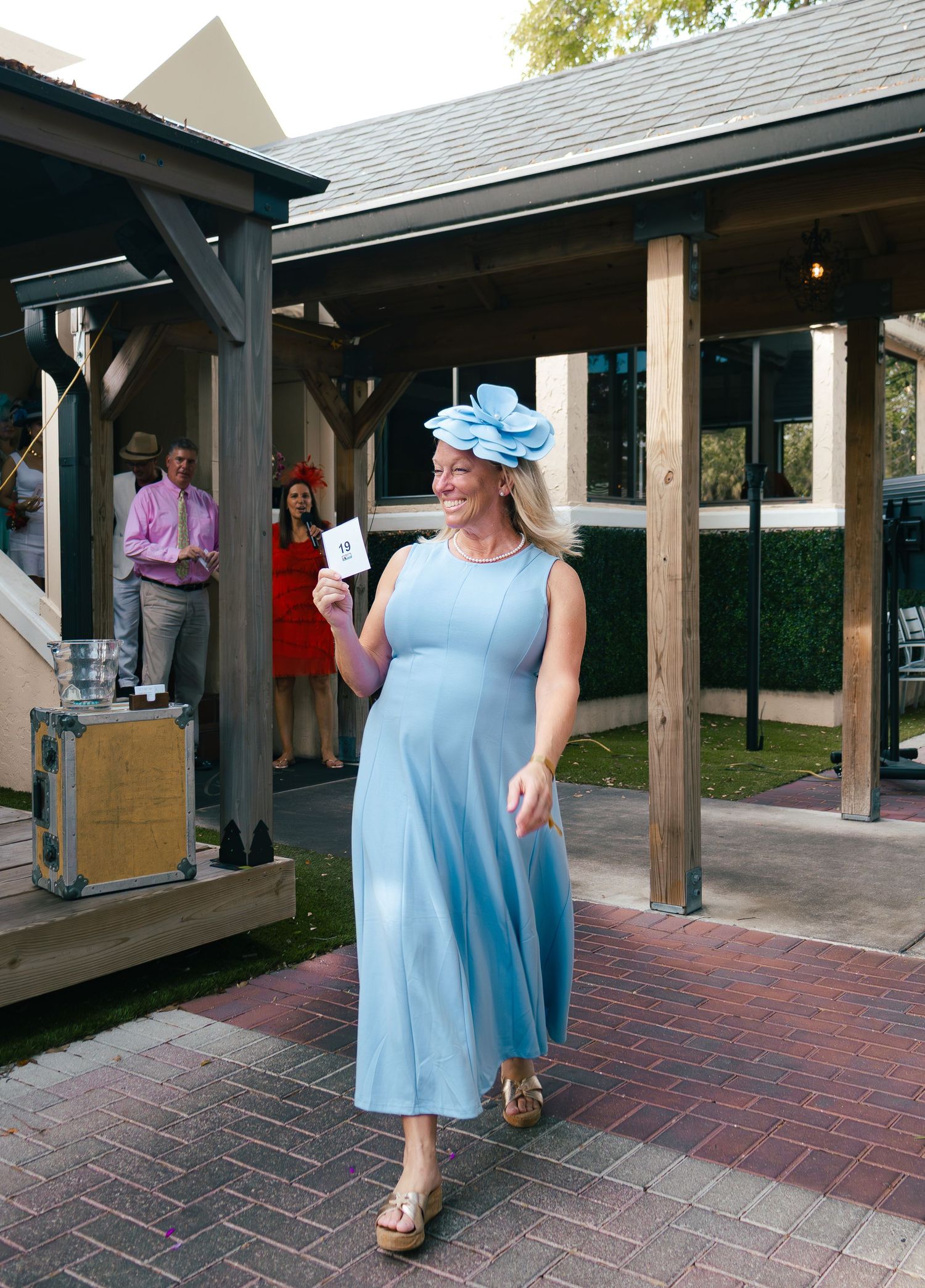 Woman in light blue dress and floral hat smiling at outdoor Kentucky Derby party event.