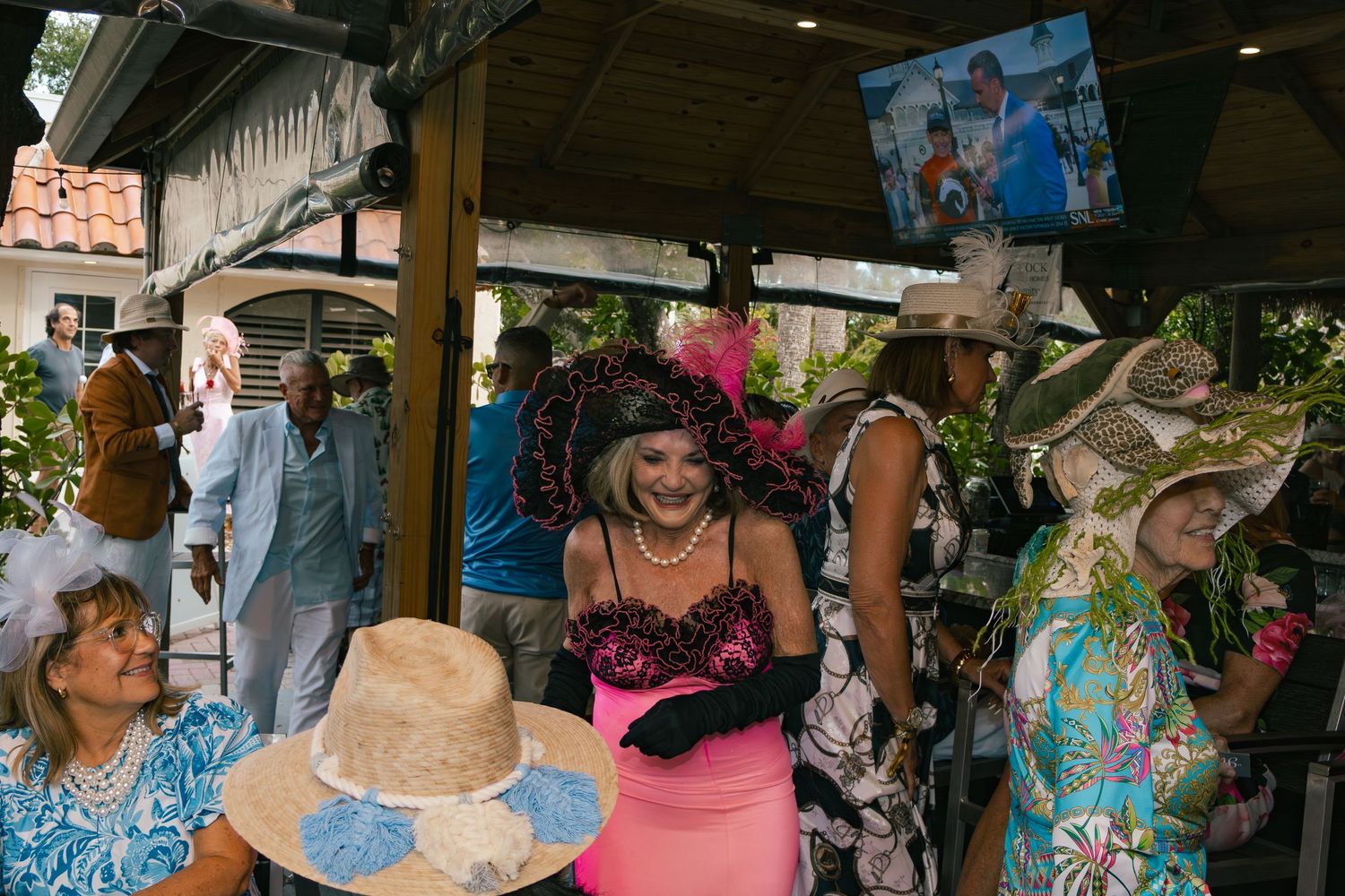 Women in elaborate decorative hats mingle at a lively Kentucky Derby themed party.