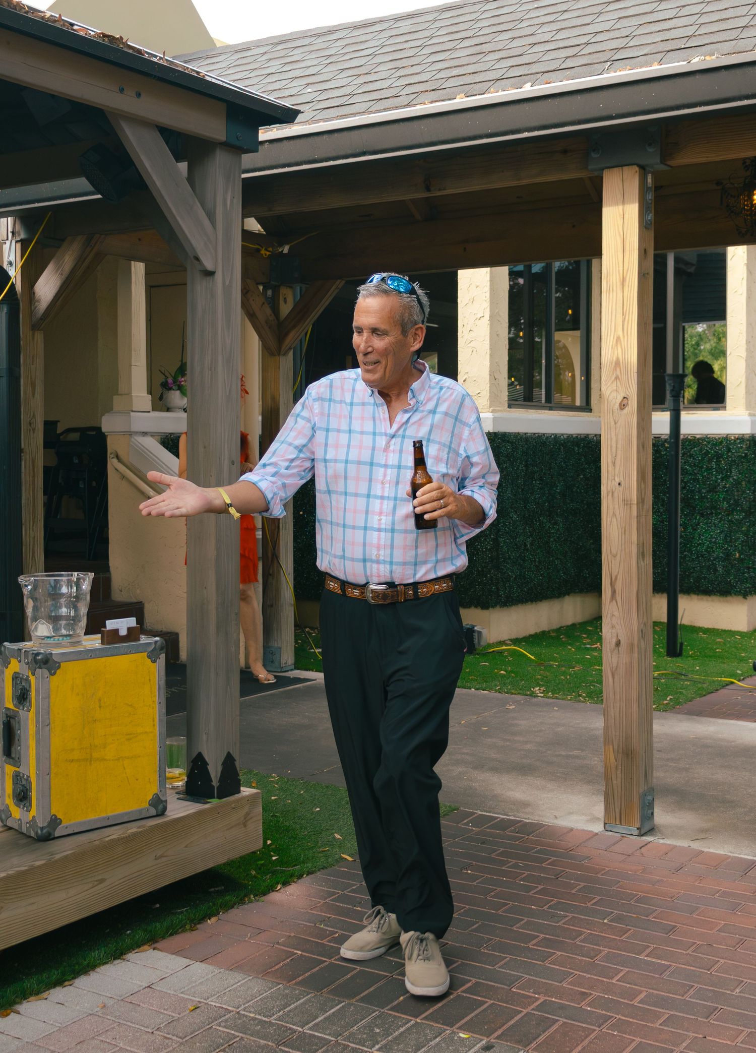 Man in plaid shirt gestures while holding beer bottle at outdoor Kentucky Derby event.