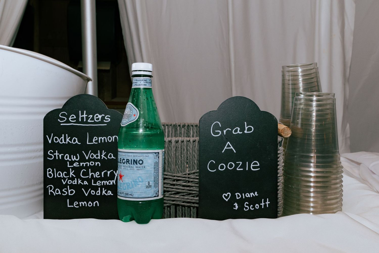 Wedding bar setup with chalkboard seltzer menu, Perrier bottle, and Grab A Coozie sign.