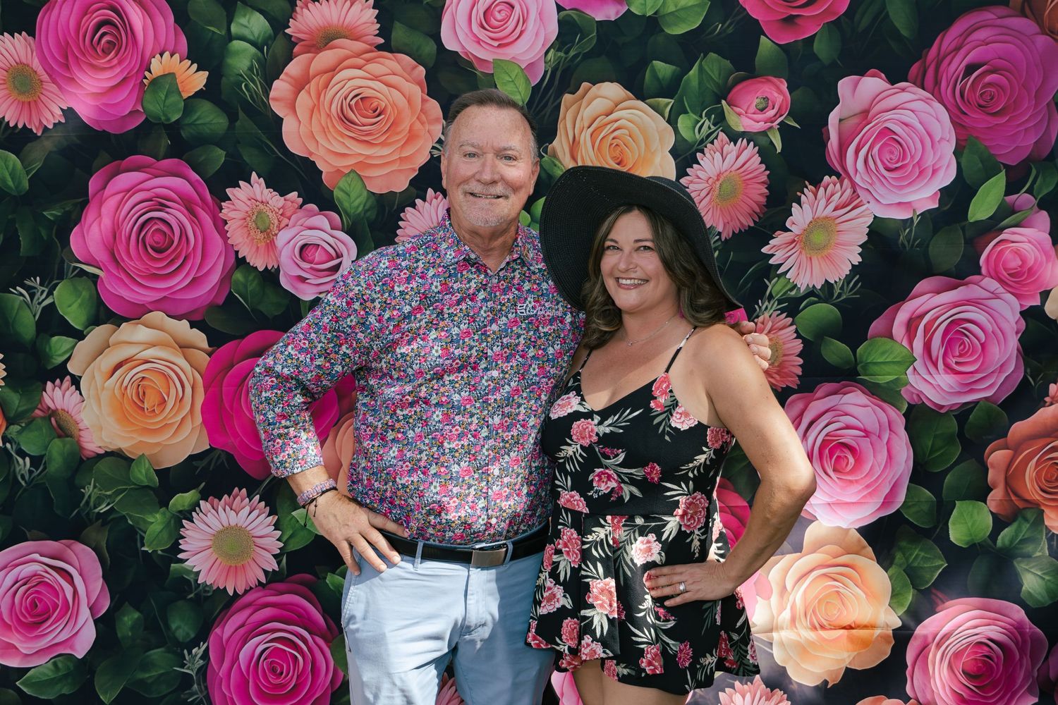 Couple smiling together in front of a vibrant floral rose backdrop at a Kentucky Derby party.