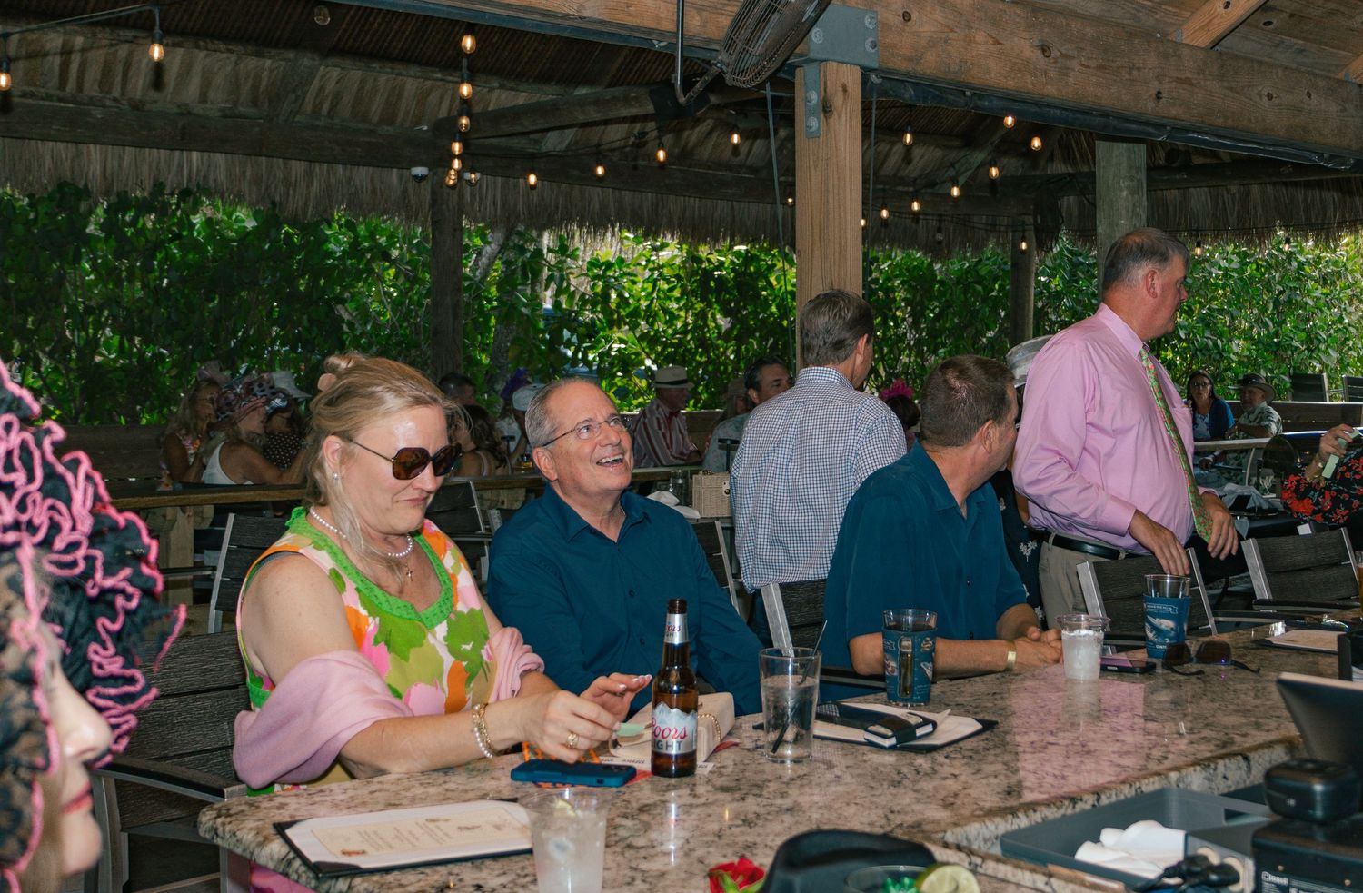 Guests in festive attire enjoy drinks and conversation at outdoor Kentucky Derby party venue.