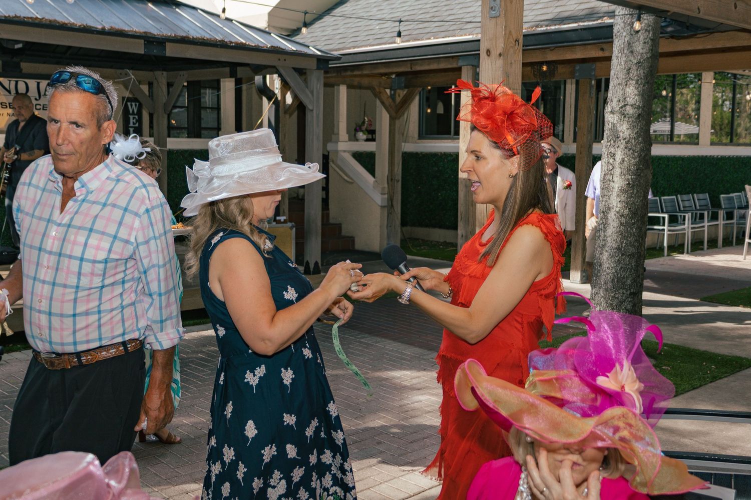 Elegantly dressed women in colorful hats and formal attire socializing at an outdoor garden party event.
