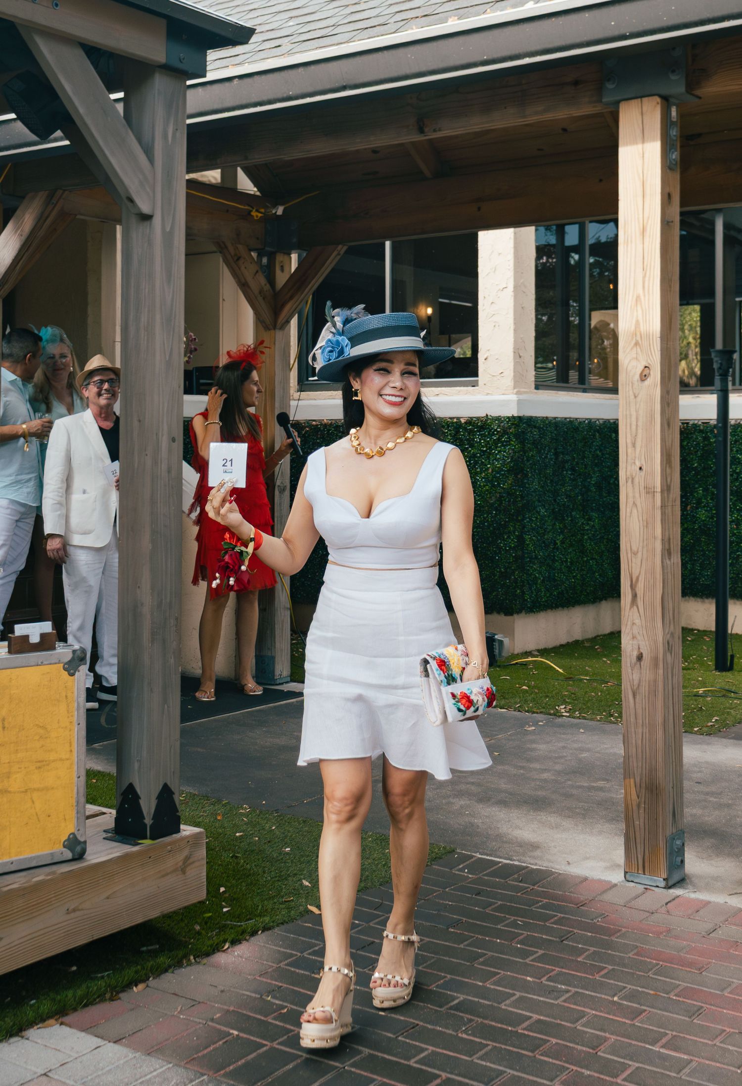Woman in white dress and blue fascinator hat smiles at an elegant outdoor Derby fashion event.