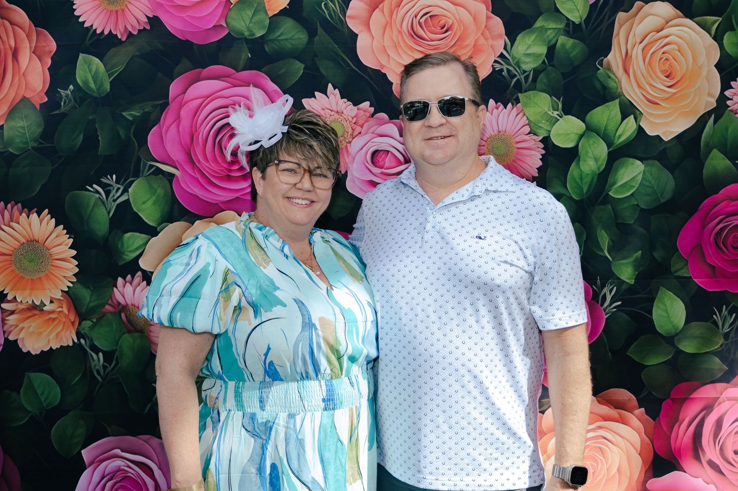 Smiling couple in casual attire posing together before a colorful painted floral rose wall backdrop outdoors.