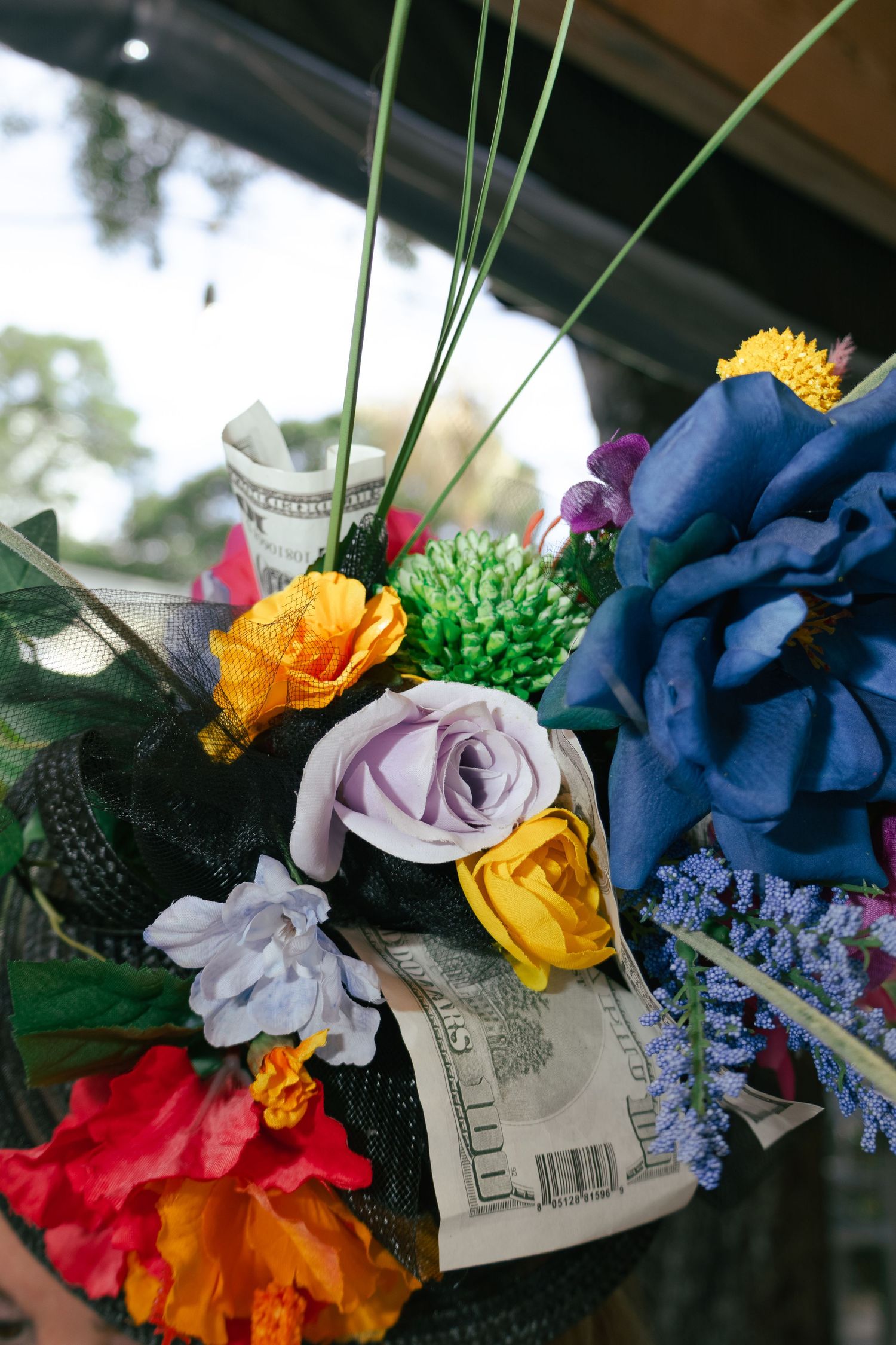 Colorful artificial flower bouquet with money bills tucked between vibrant silk roses and blooms.