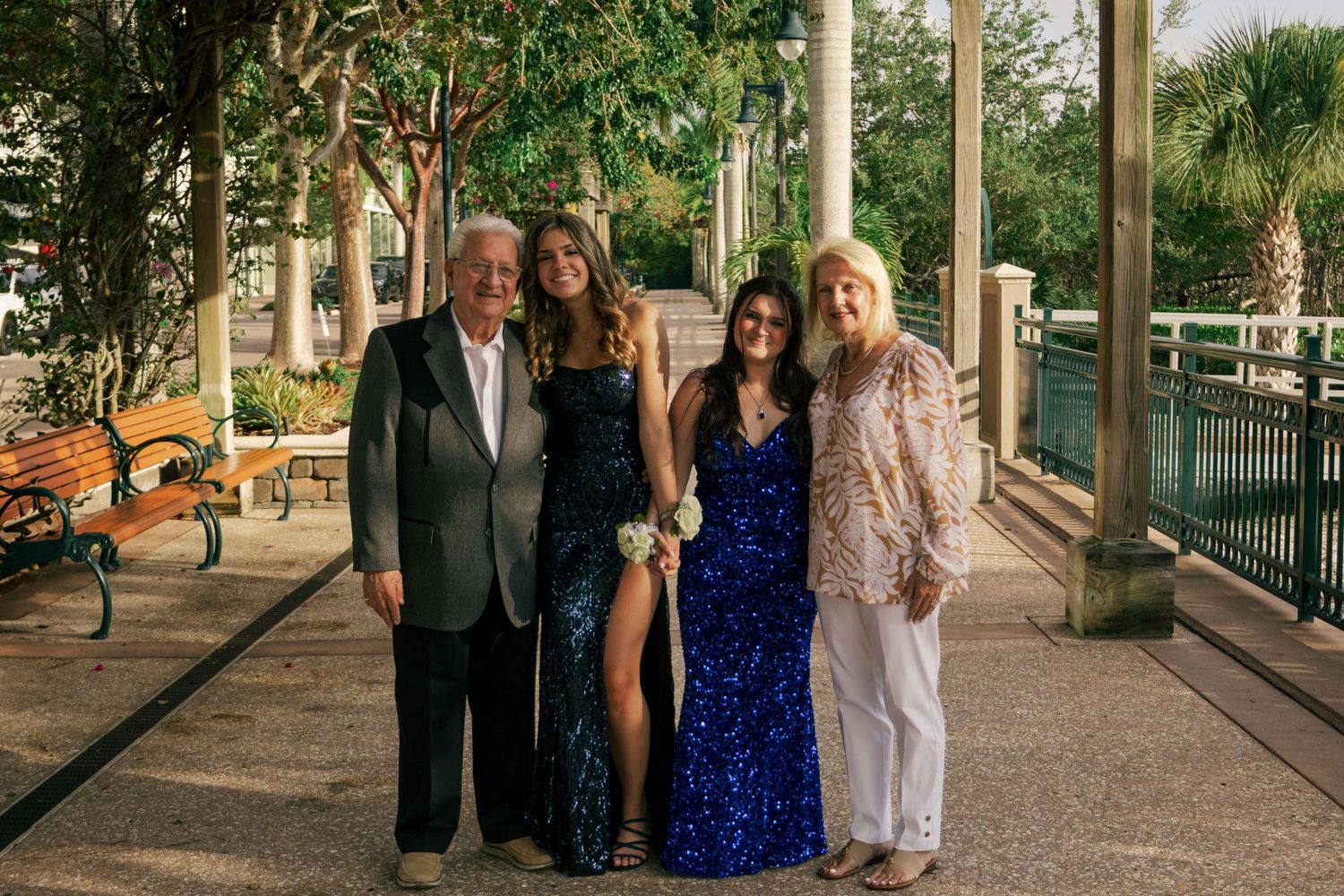 Two elegantly dressed young women pose with an older couple at a formal outdoor event.