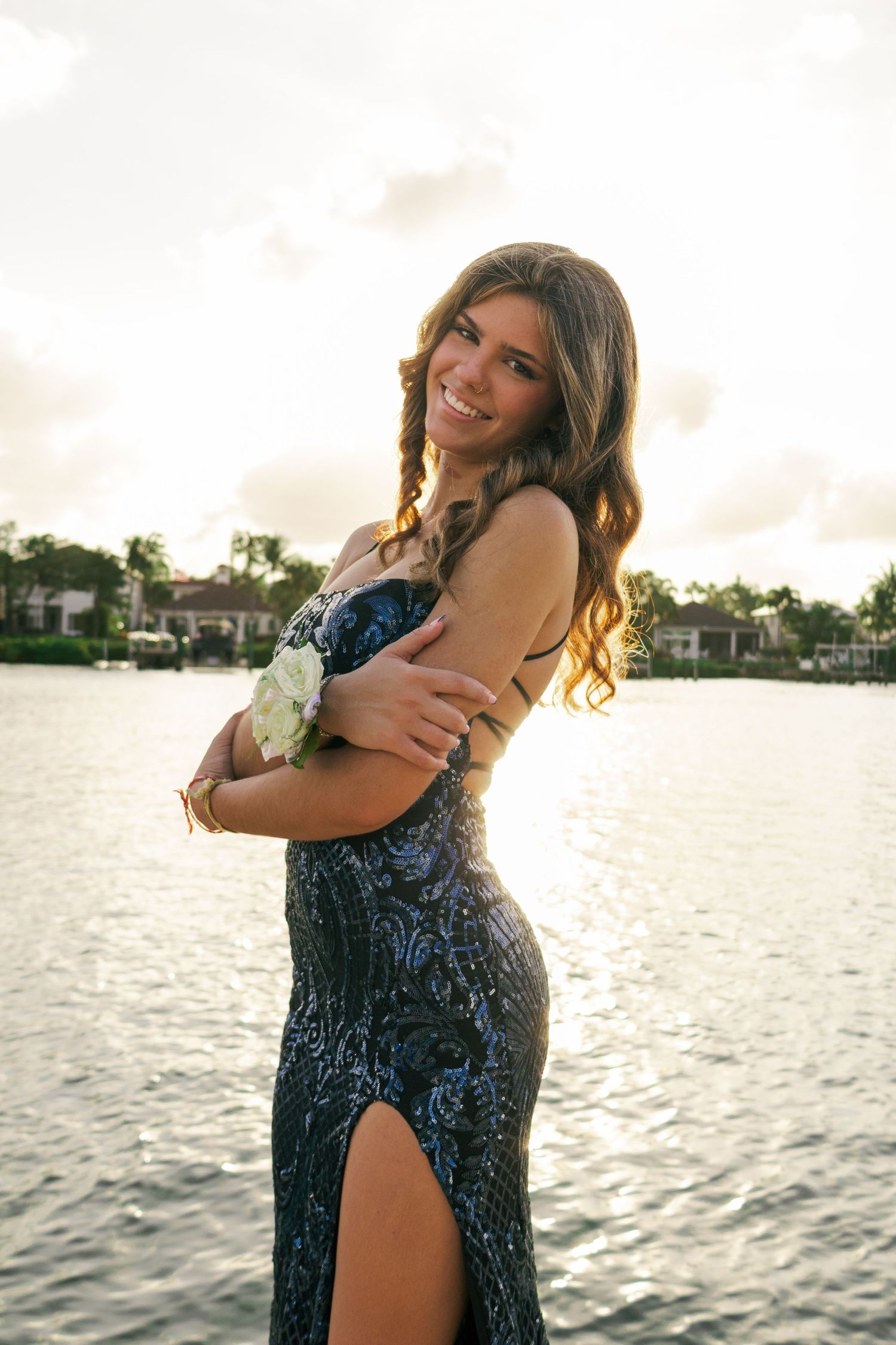 Teenage girl in navy blue sequin dress with slit smiles while posing by sparkling waterfront.