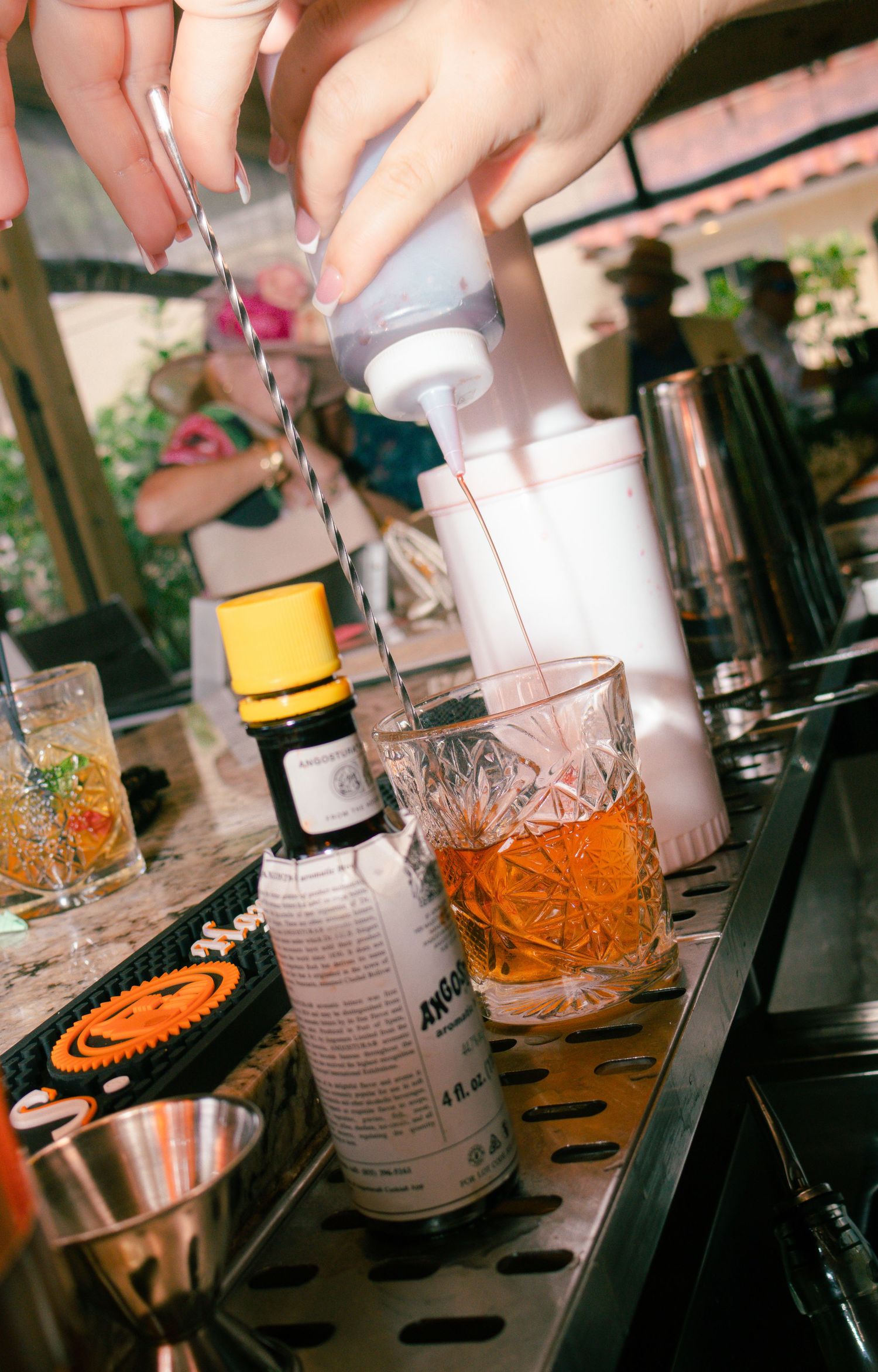 Bartender adding bitters to an old fashioned cocktail at an outdoor bar event.