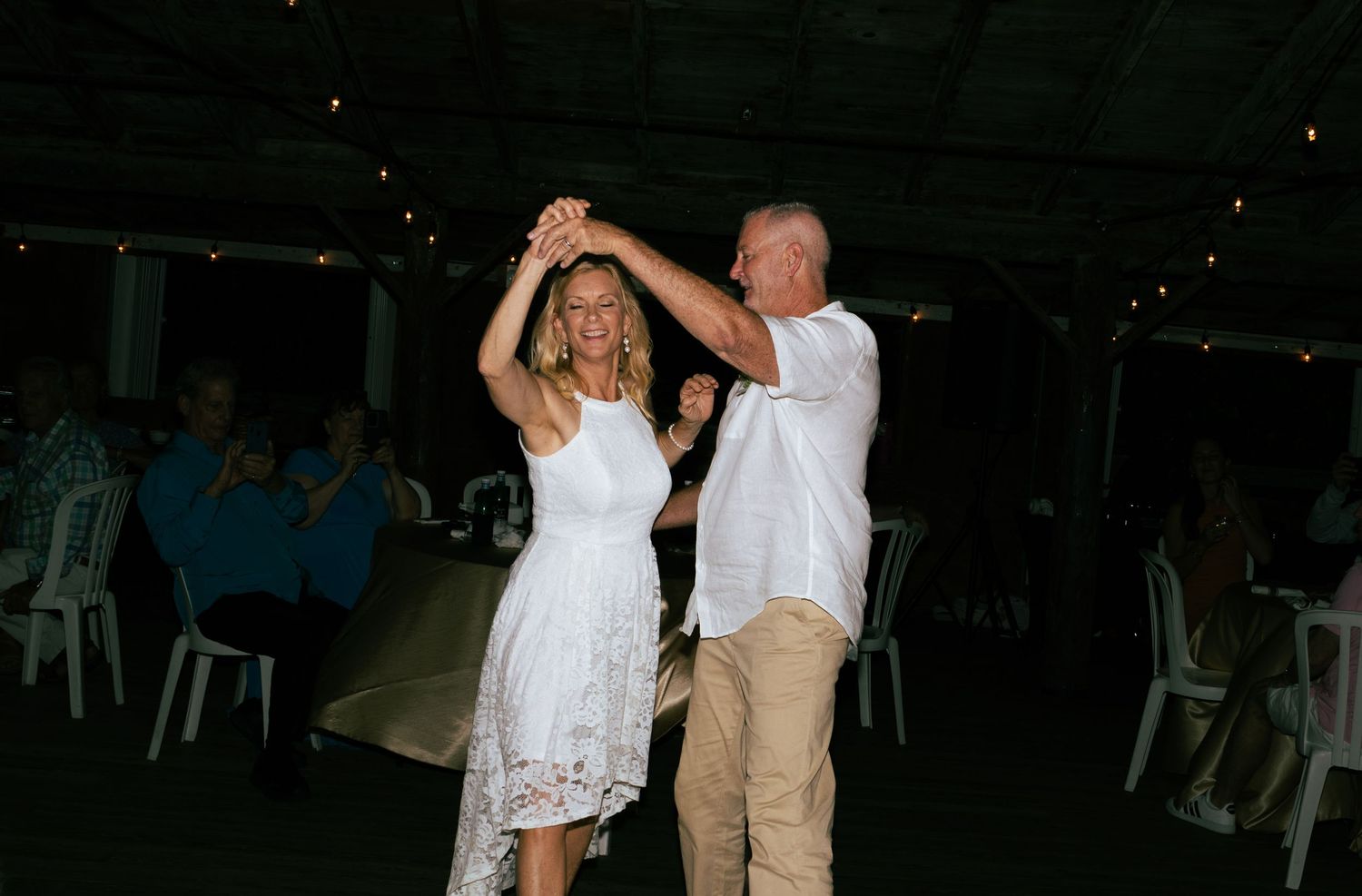 Newlyweds dancing together as guests applaud at their evening wedding reception.