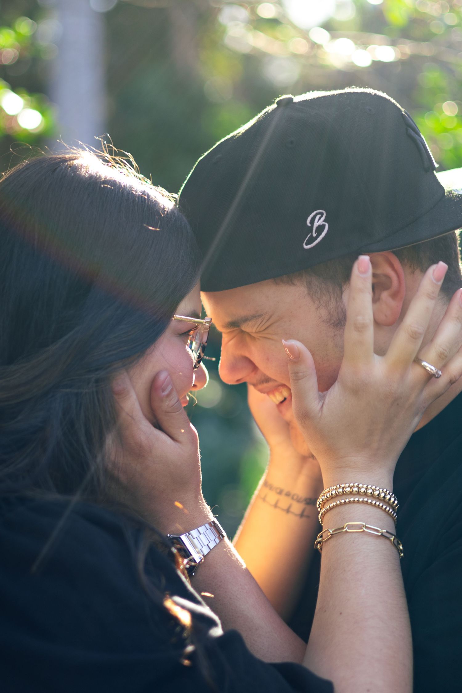 A joyful couple nearly kissing outdoors in golden sunlight, woman holding mans face while both smile warmly.