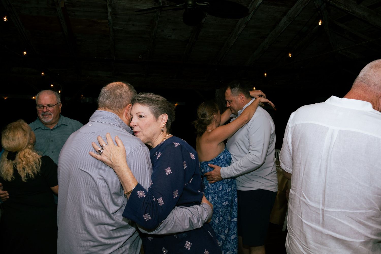 Guests slow dancing together at an outdoor evening wedding celebration.