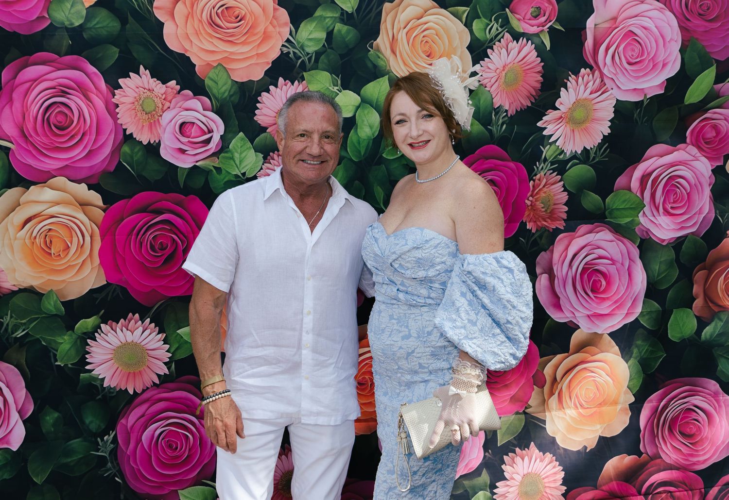 Man and woman posing together in front of a colorful floral rose wall backdrop at an event.