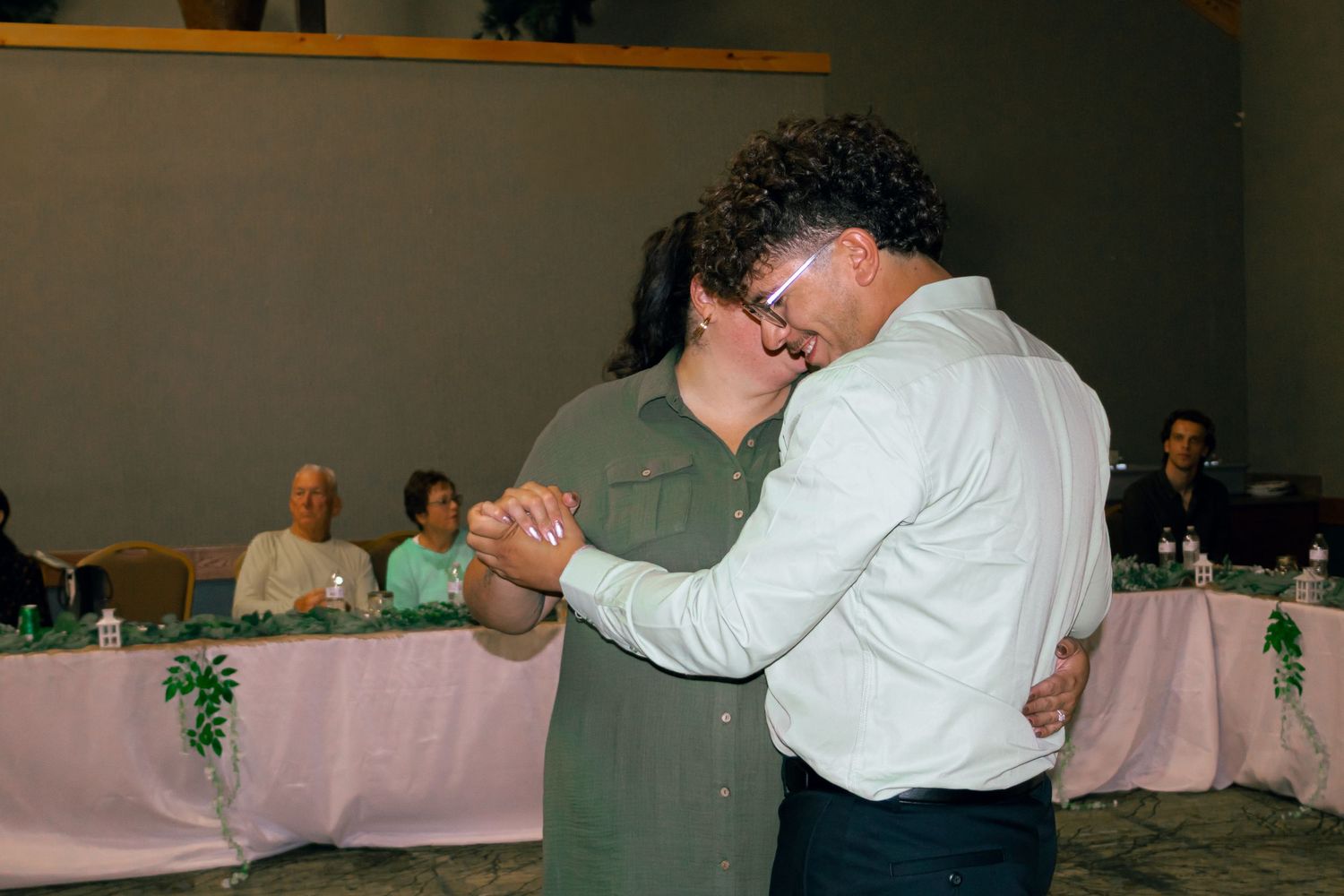 Couple sharing a slow dance at a wedding reception with guests watching.
