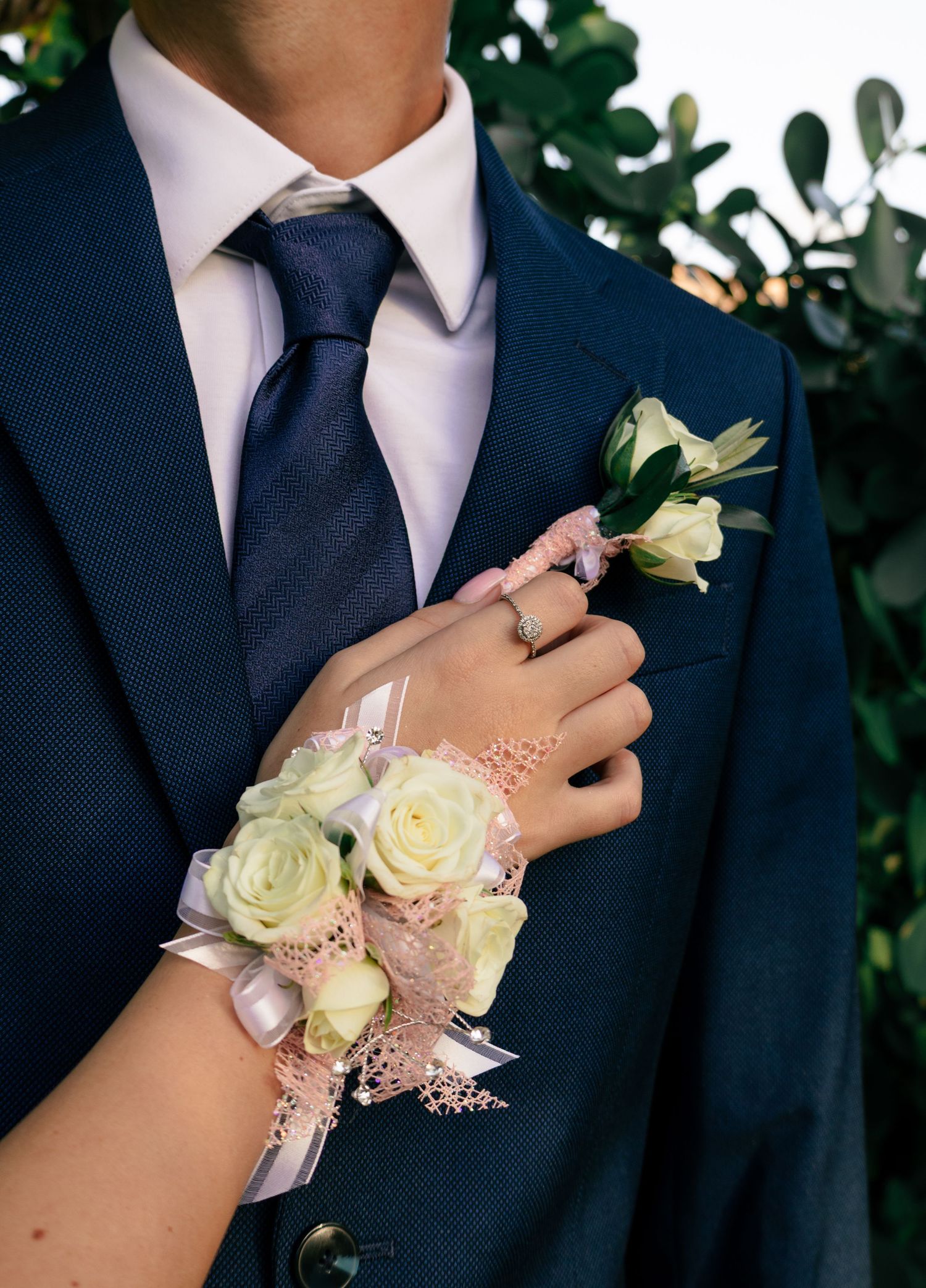 Close-up of a wrist corsage with white roses next to a matching boutonniere on a navy suit.