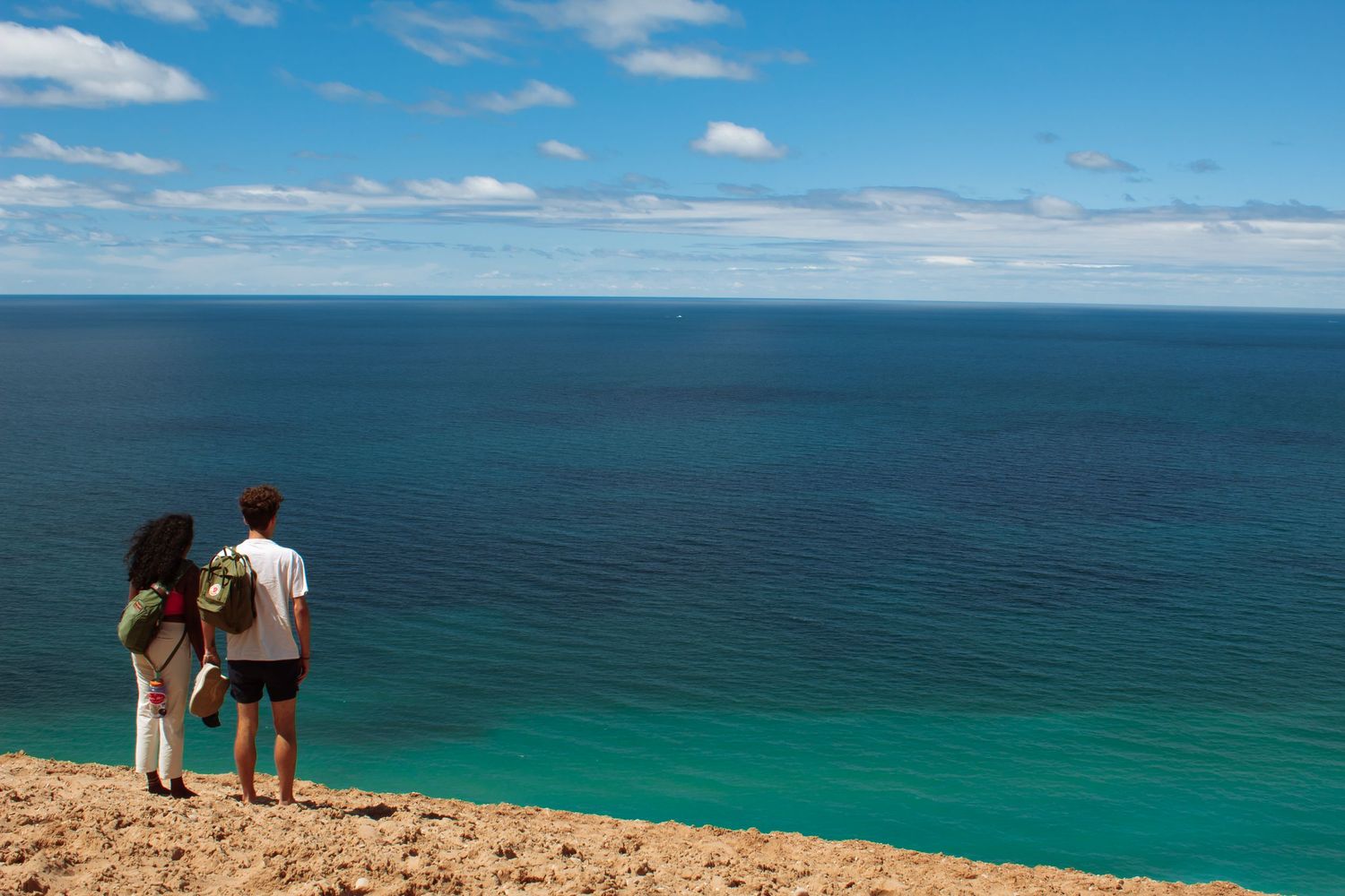 Couple standing on a cliff overlooking a stunning turquoise ocean vista.