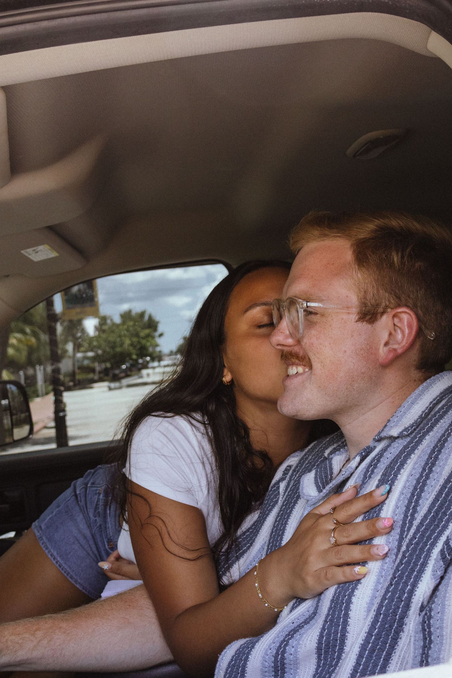 Woman kissing her boyfriend on the cheek while sitting together inside a car.