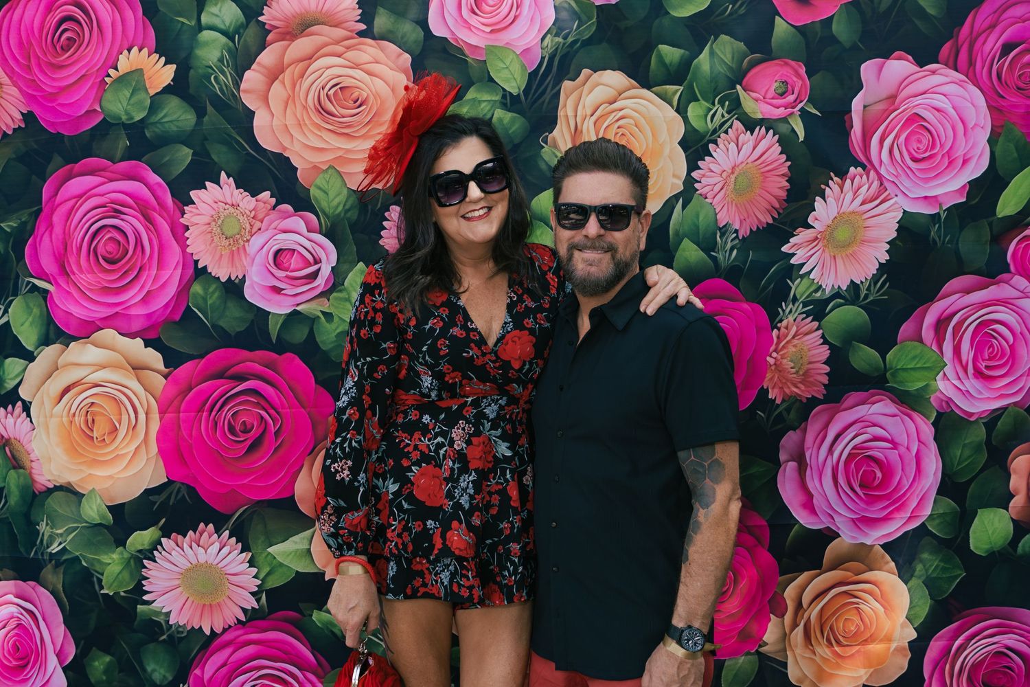 Couple in floral outfits posing together in front of a vibrant painted rose backdrop.