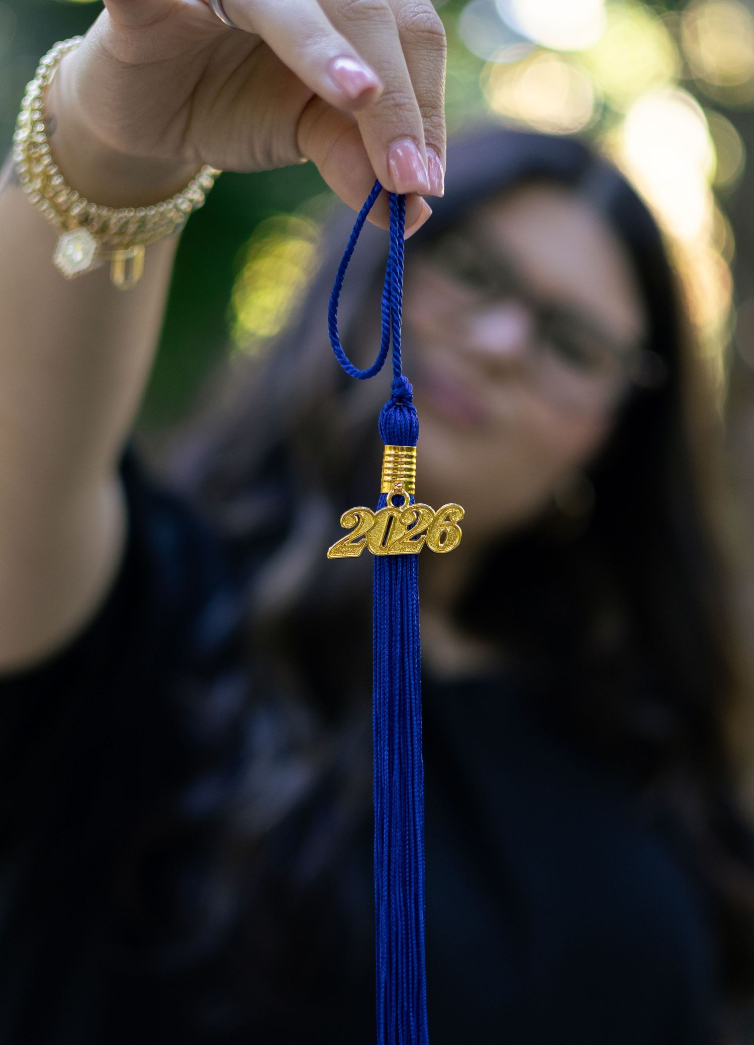 Close-up of 2026 graduation tassel held up by young woman in outdoor bokeh background.