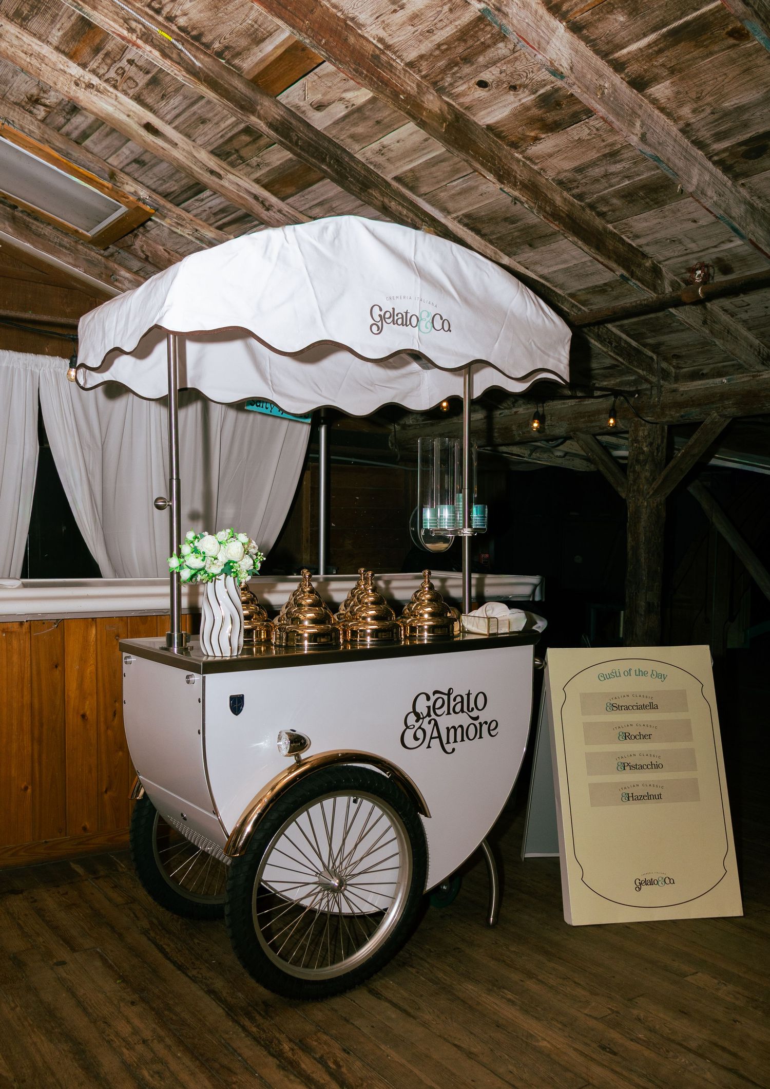 Elegant Gelato e Amore cart with gold dispensers and white umbrella at wedding reception.