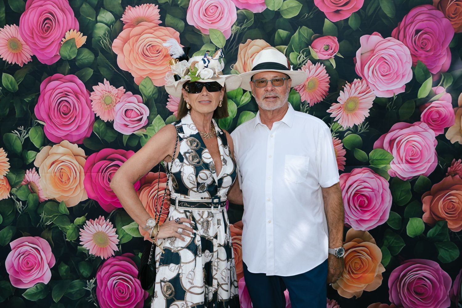 Stylish couple in black-and-white dress and white linen outfit posing before a vibrant painted floral backdrop.