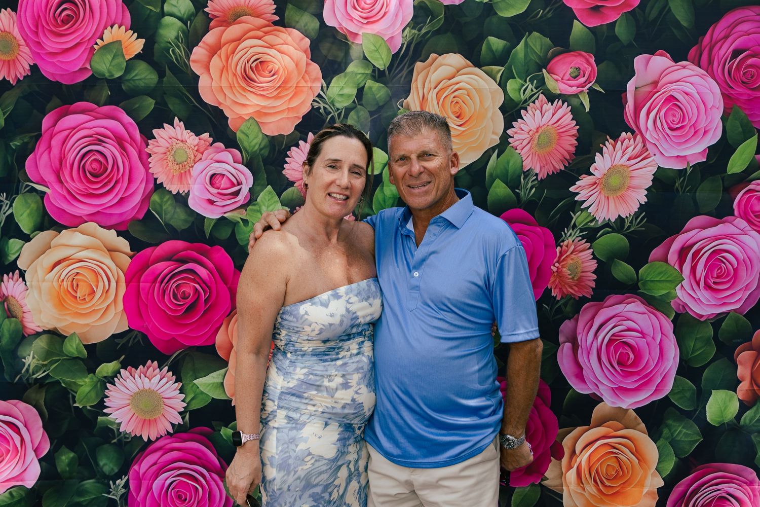 Smiling couple posing together in front of a colorful floral rose backdrop at a Kentucky Derby party.