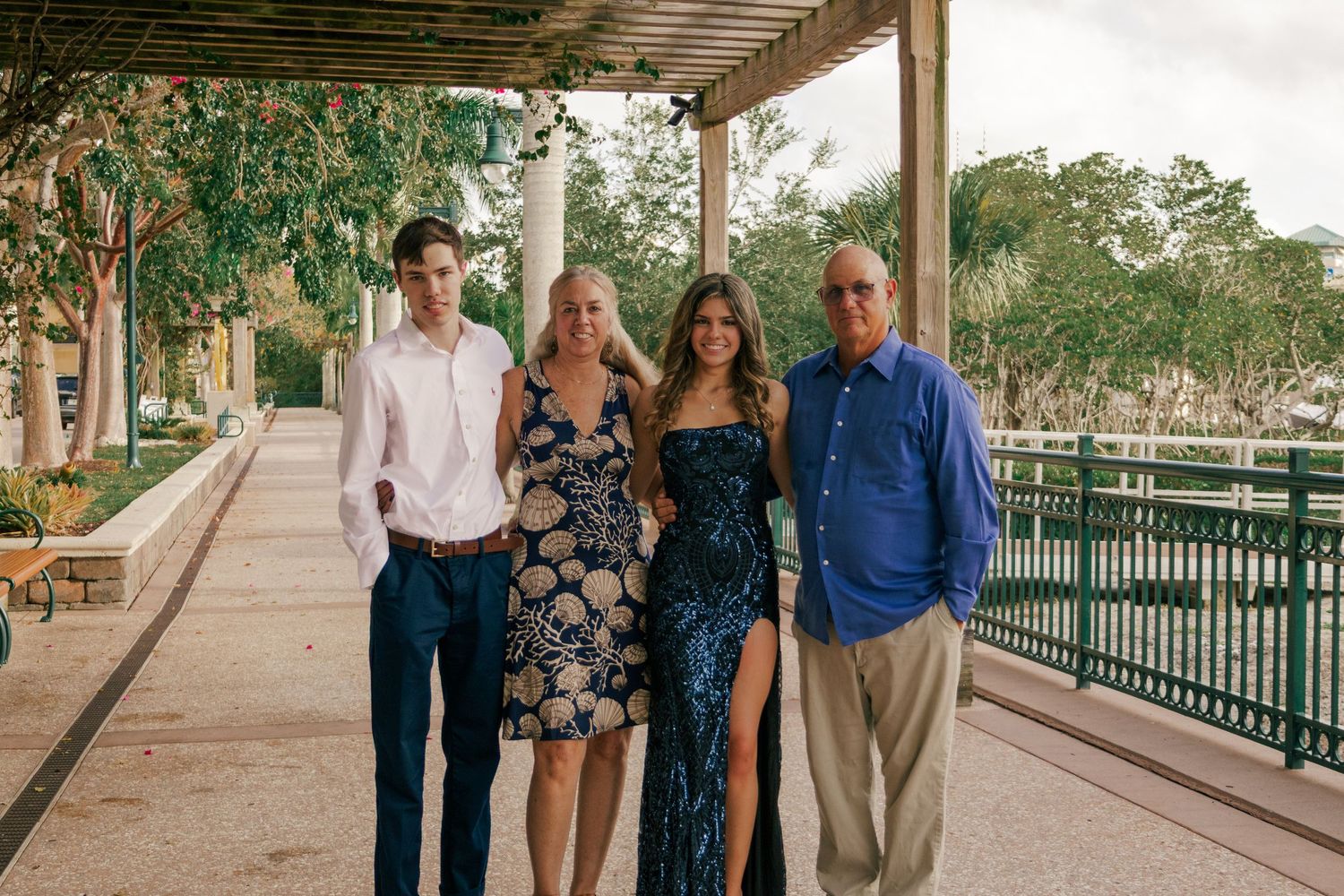 Smiling family of four standing together under a pergola walkway at a scenic outdoor venue.