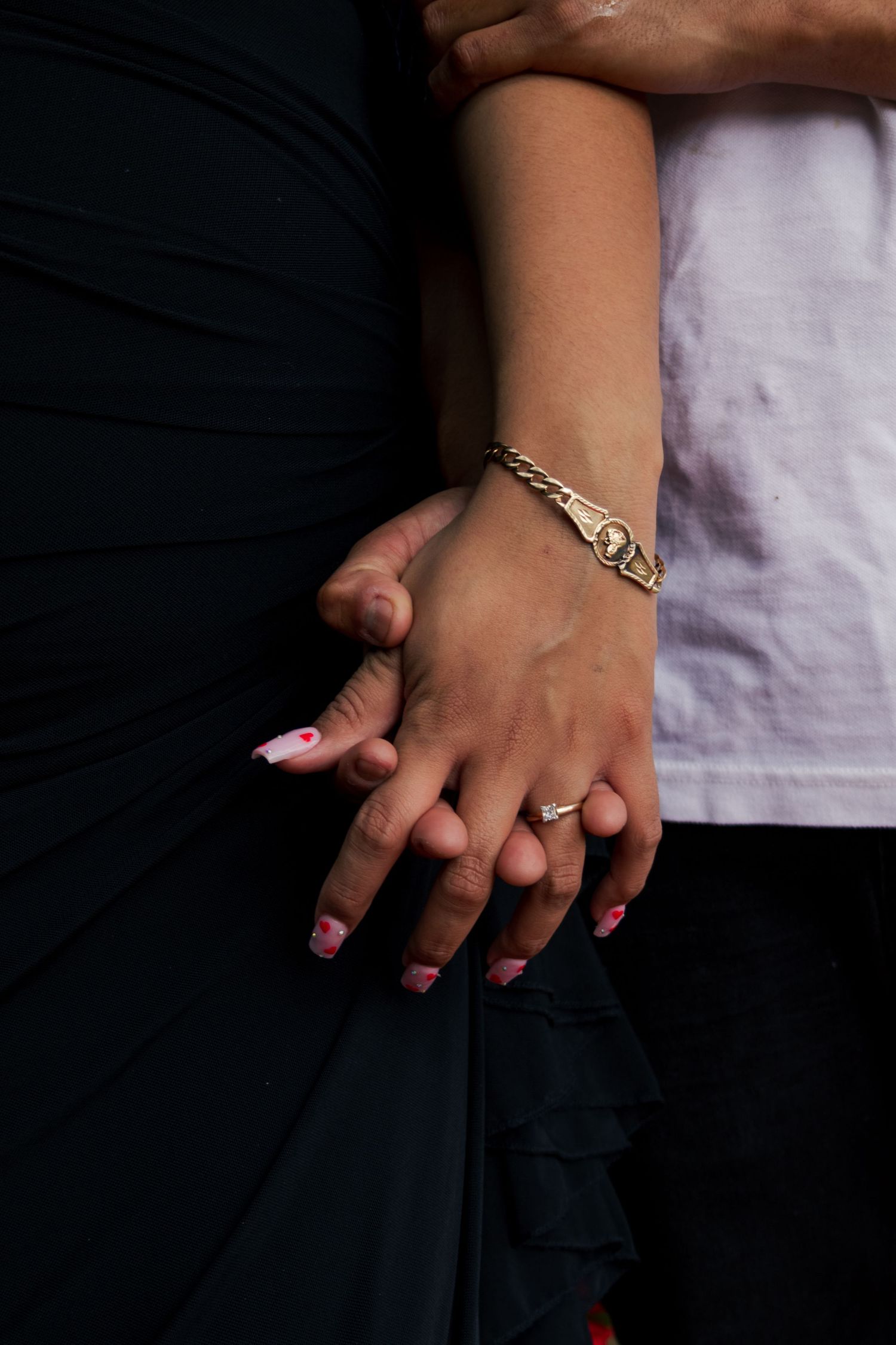 Close-up of couple holding hands showing an engagement ring and gold bracelet.