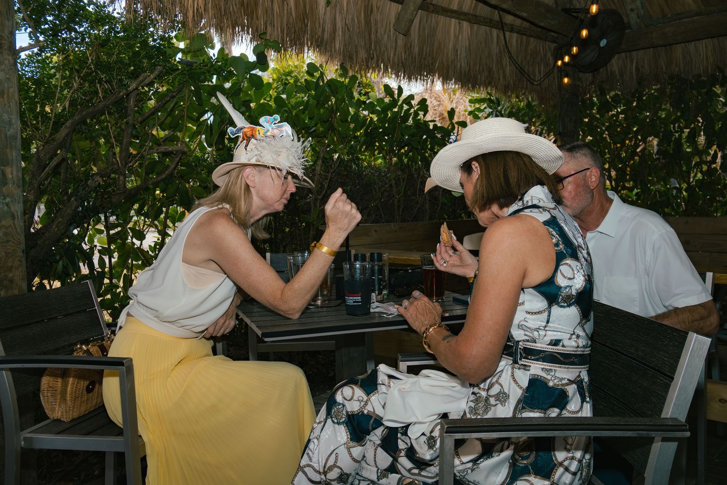 Two women in festive hats engage in animated conversation at an outdoor dining table.