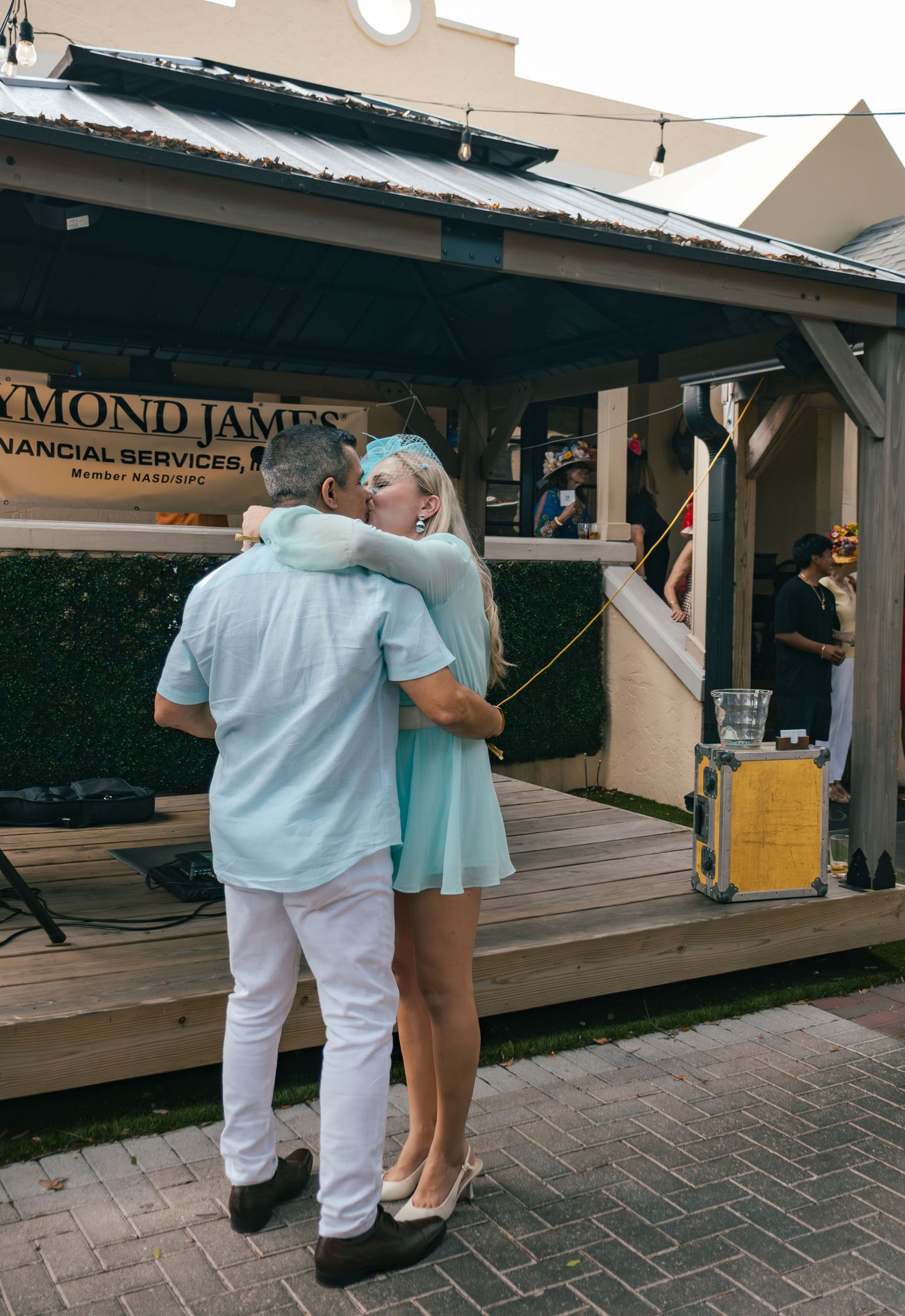 Couple embracing near Raymond James Financial Services sign at outdoor Derby event.