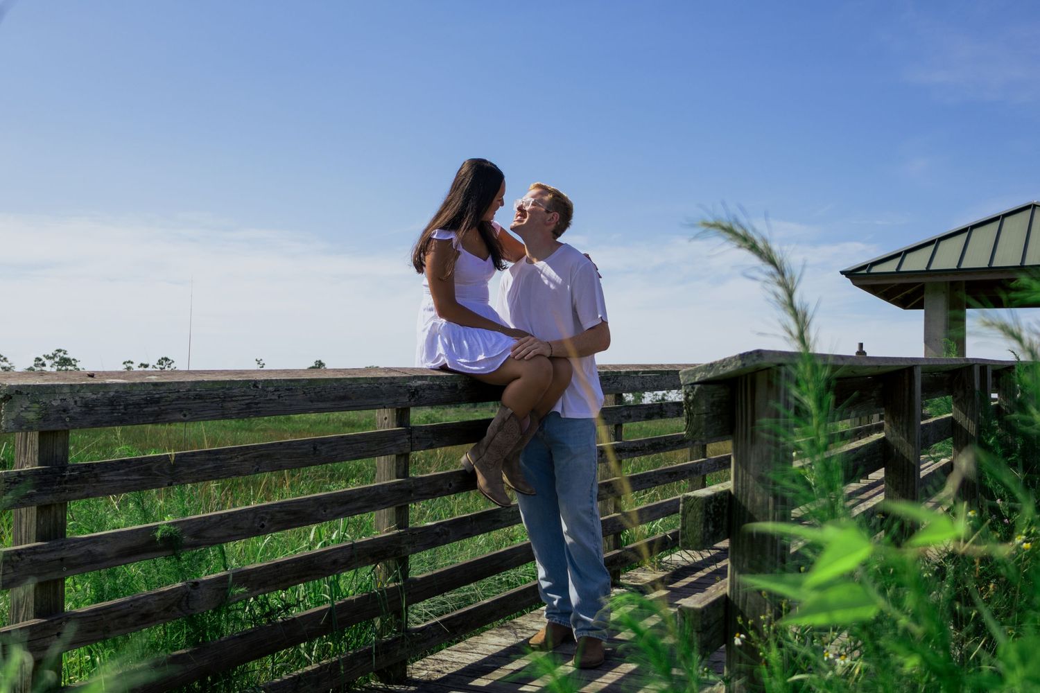 Romantic couple sharing a tender moment on a wooden fence overlooking a green meadow.