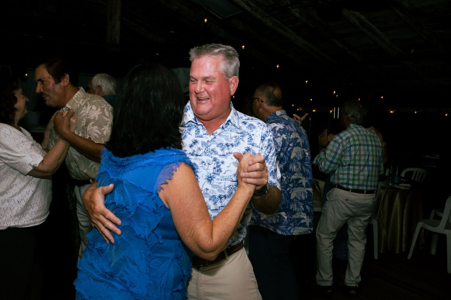 Man in floral shirt dancing with woman in blue dress at outdoor reception.