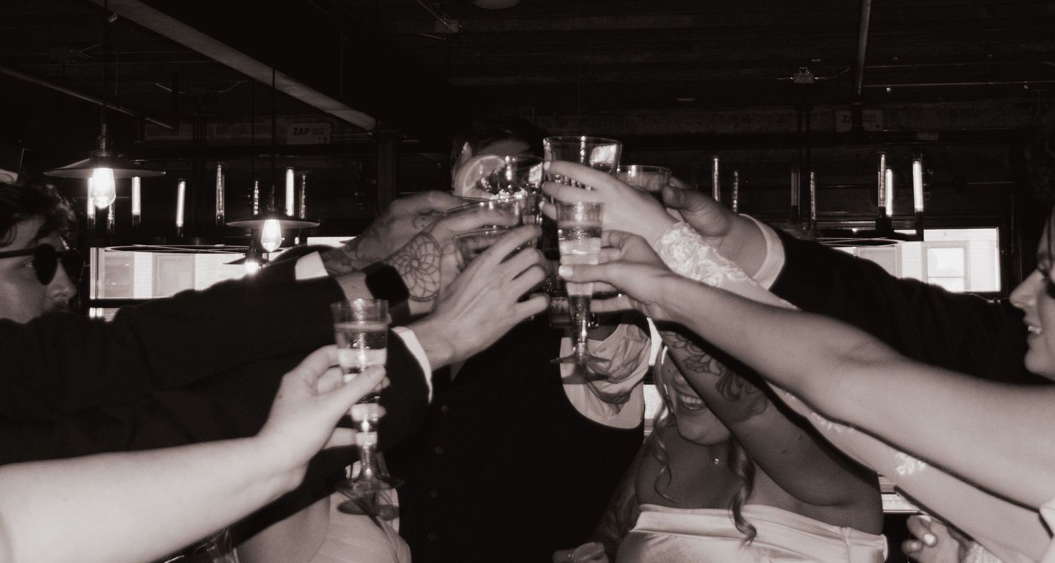 Wedding guests raise glasses in a celebratory toast at the reception bar.