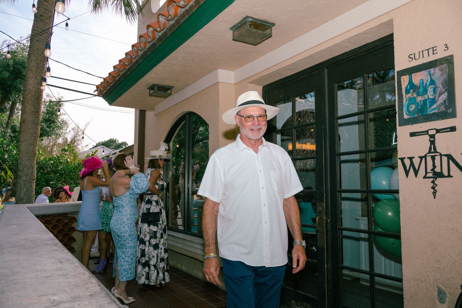 Man in white hat and shirt standing outside a suite entrance at a tropical venue.