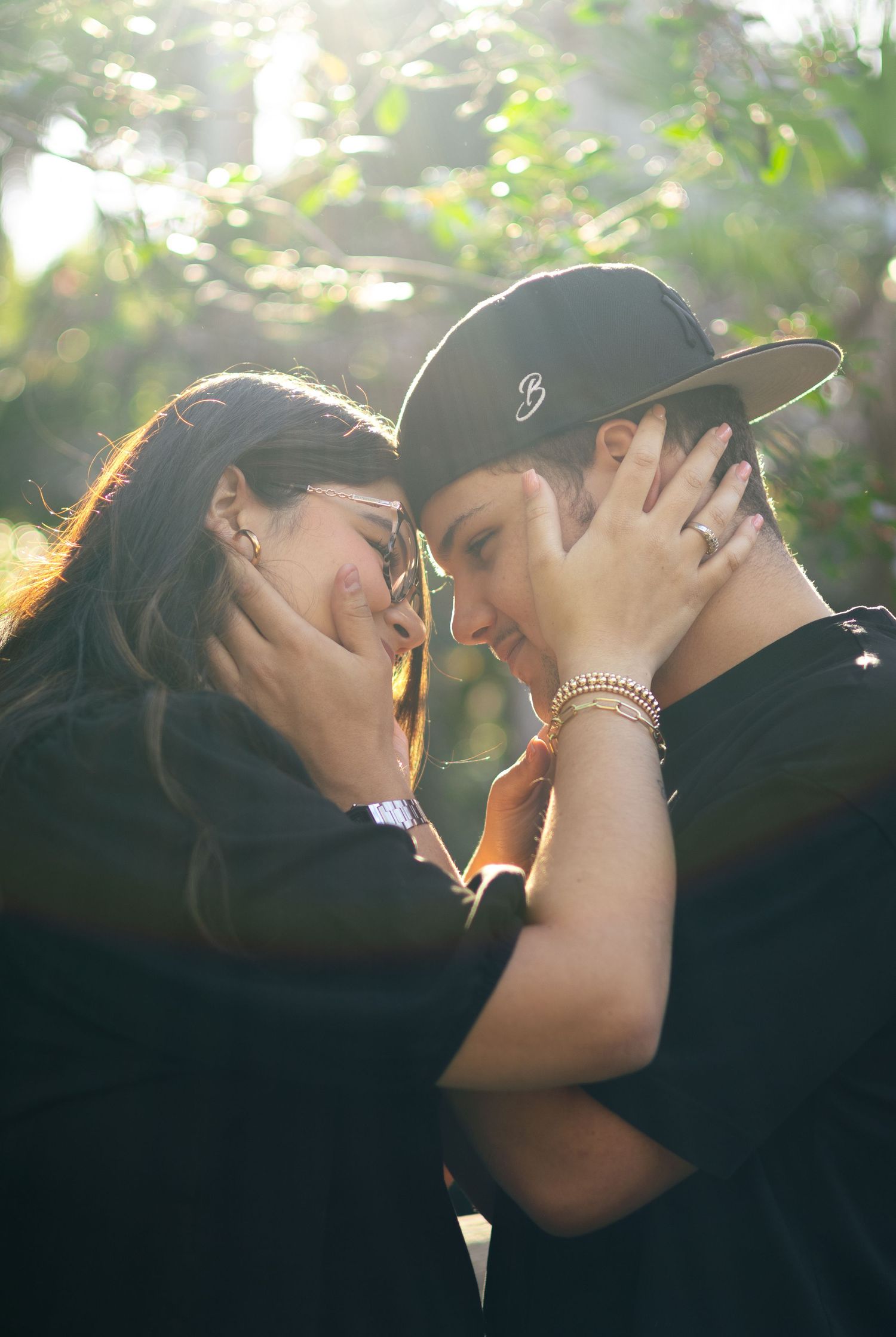 Romantic couple sharing an intimate moment outdoors with soft sunlight filtering through trees.