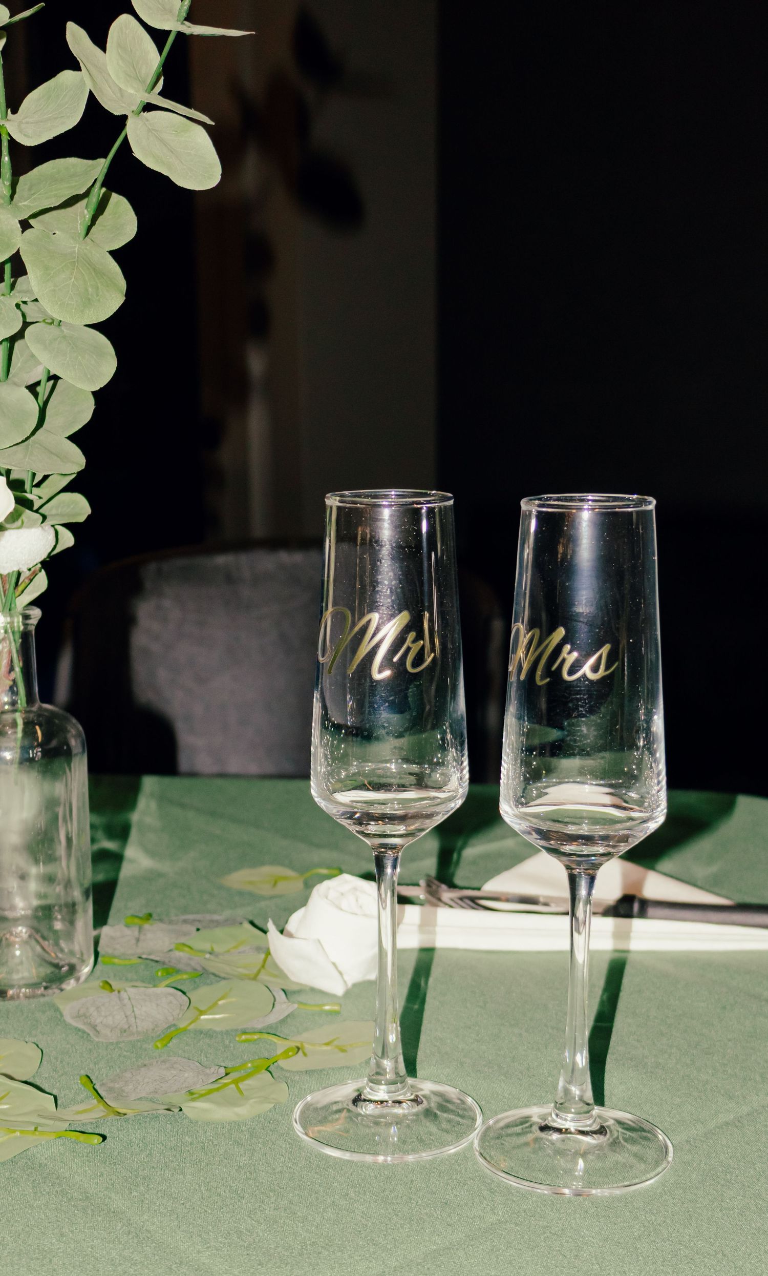 Mr and Mrs wedding champagne flute glasses on green table with eucalyptus decor.